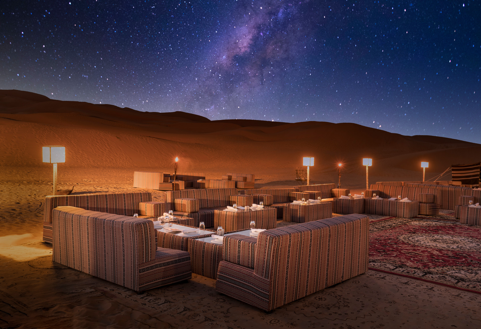 Illuminated sofas and tables set for dinner under milky way in a luxury desert camp