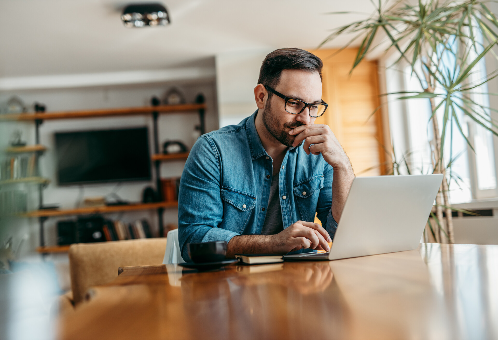 Pensive man looking at laptop while sitting at wooden table, portrait.