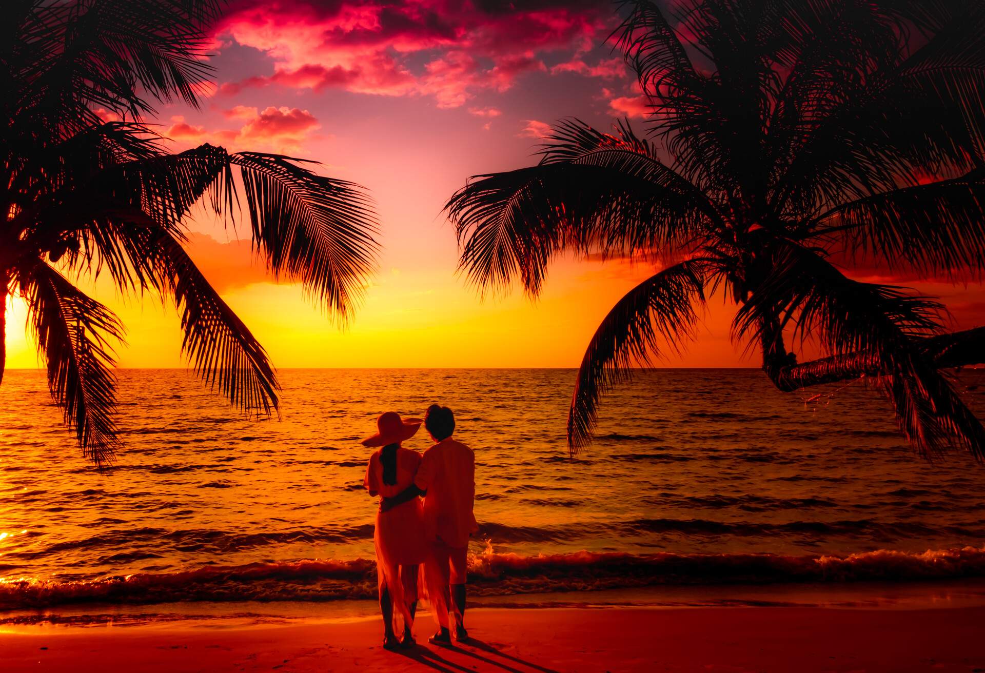 A couple on the shore of a tropical beach against the scenic sunset sky.