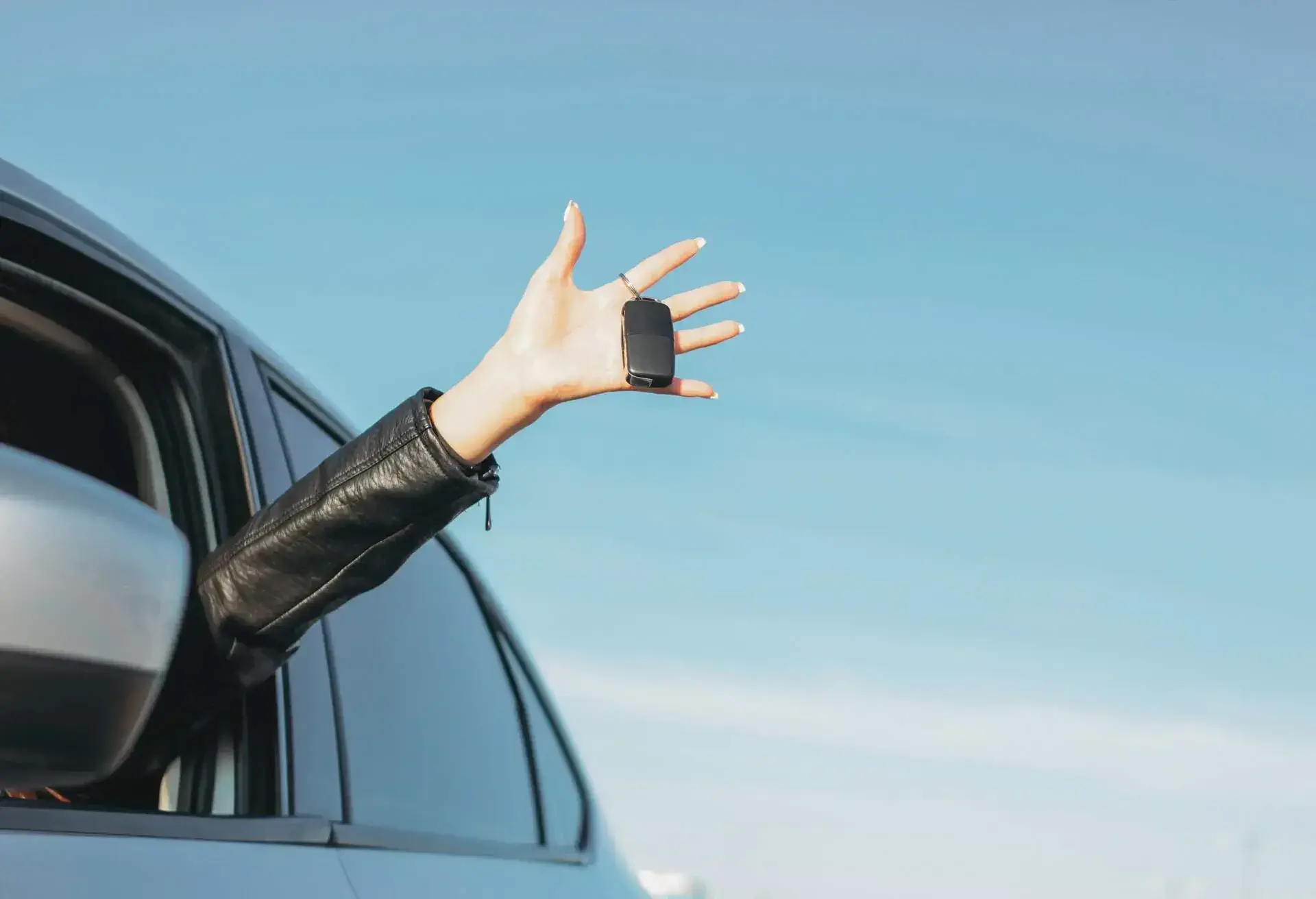 A person's hand is coming out of a car window holding a car key