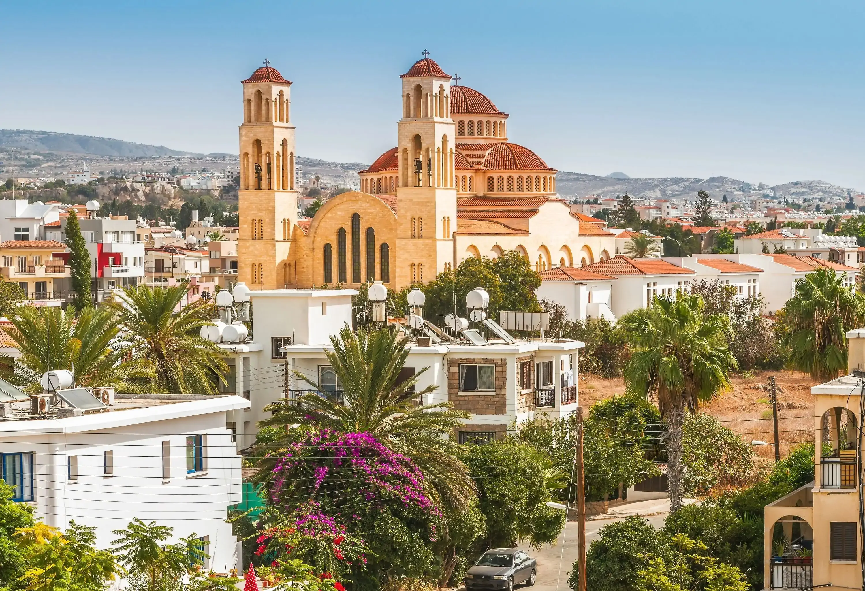 A church's domed roofing and towers dominate the skyline of a city filled with palm trees and buildings.