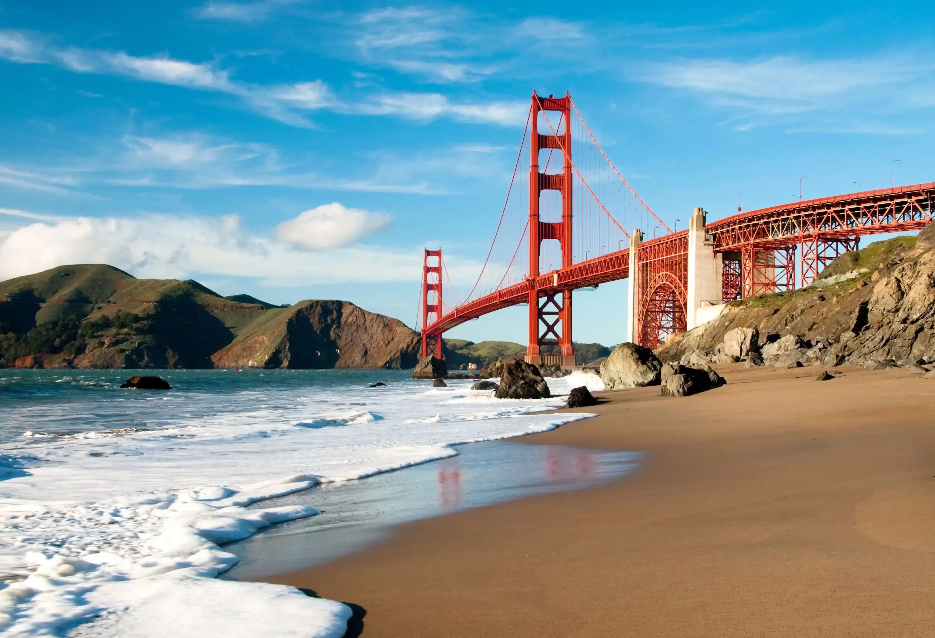 Frothy waves sweeping across the dense sand along the shore of San Francisco Bay.