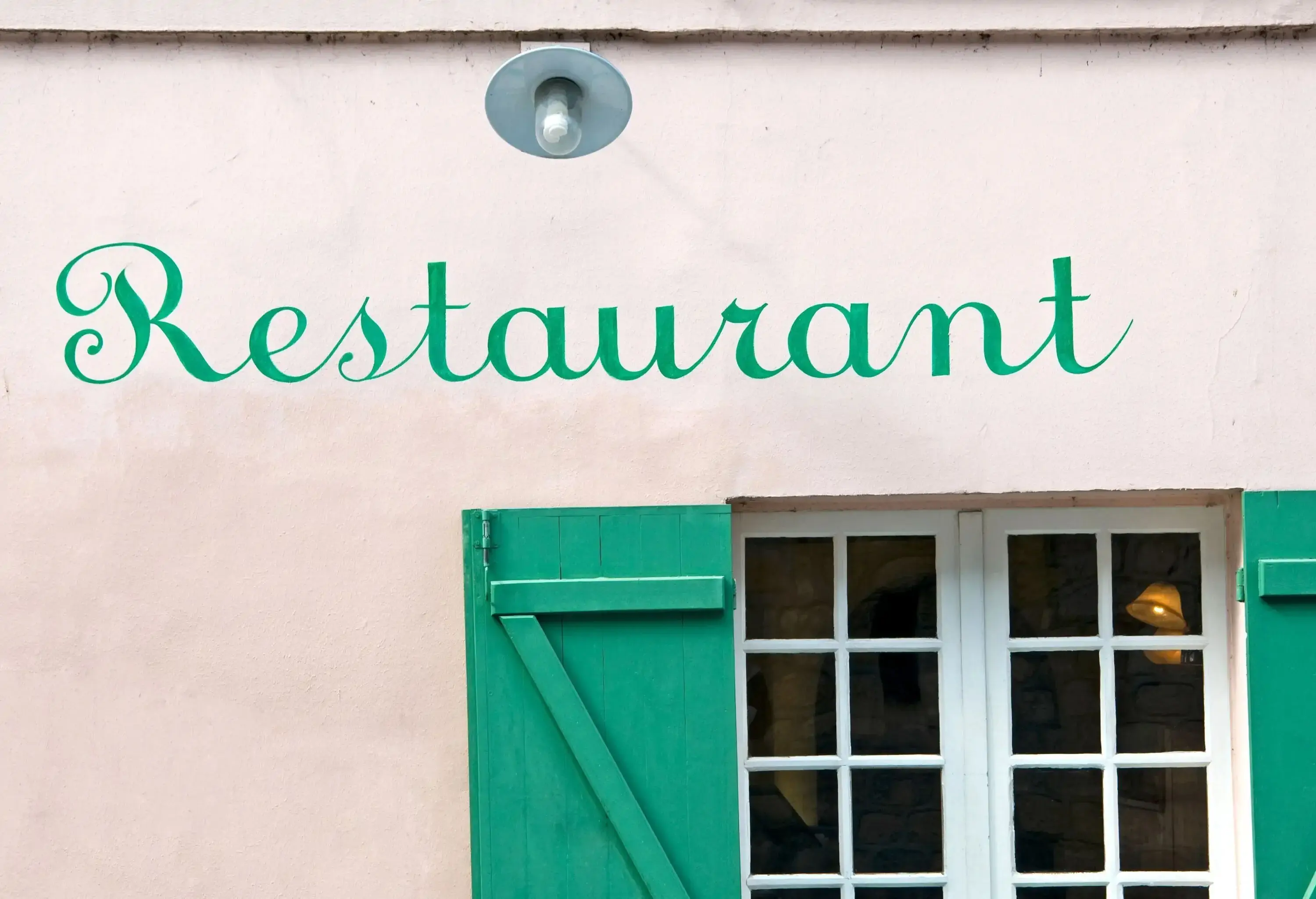 A structure with glass windows and wooden shutters and the word "Restaurant" written above it.