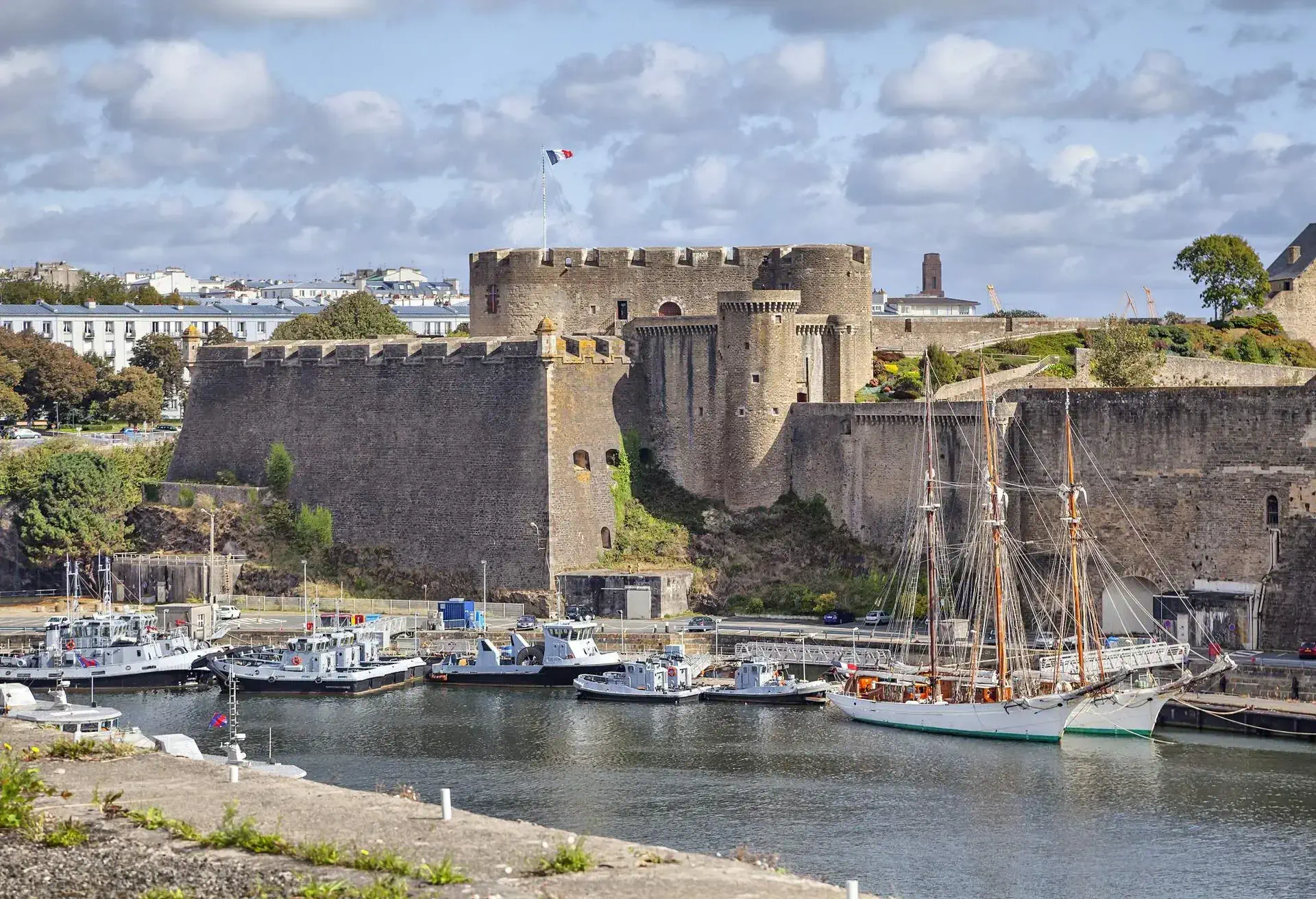 A castle with high walls beside a harbour with anchored boats.