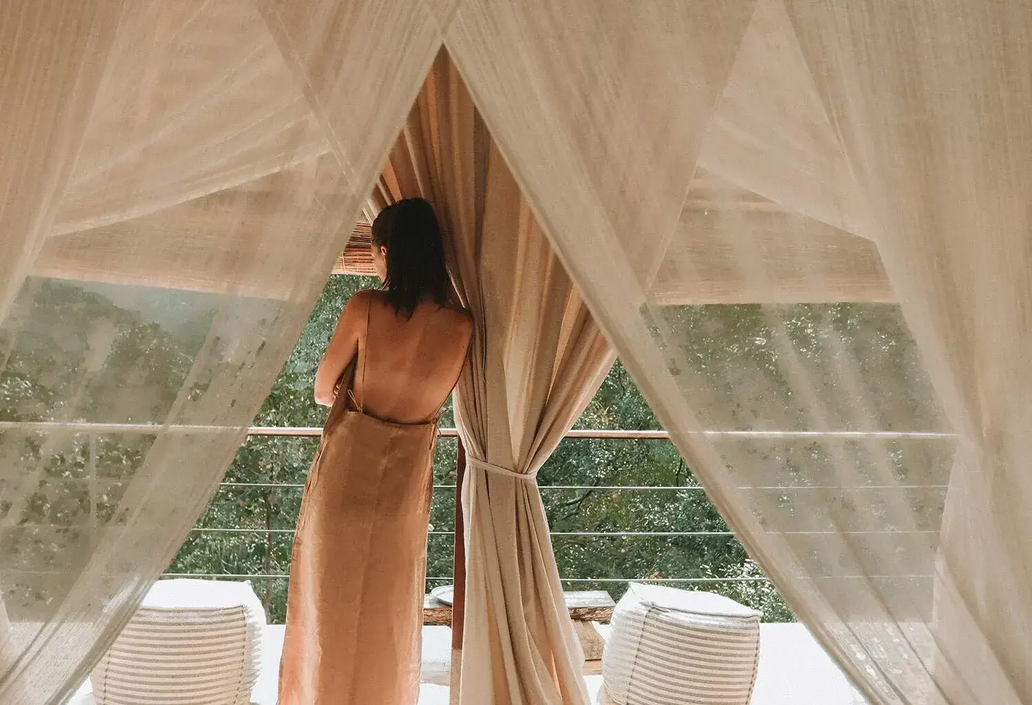 A woman leaning on a balcony railing of a contemporary hotel room, enjoying the scenic forest view.