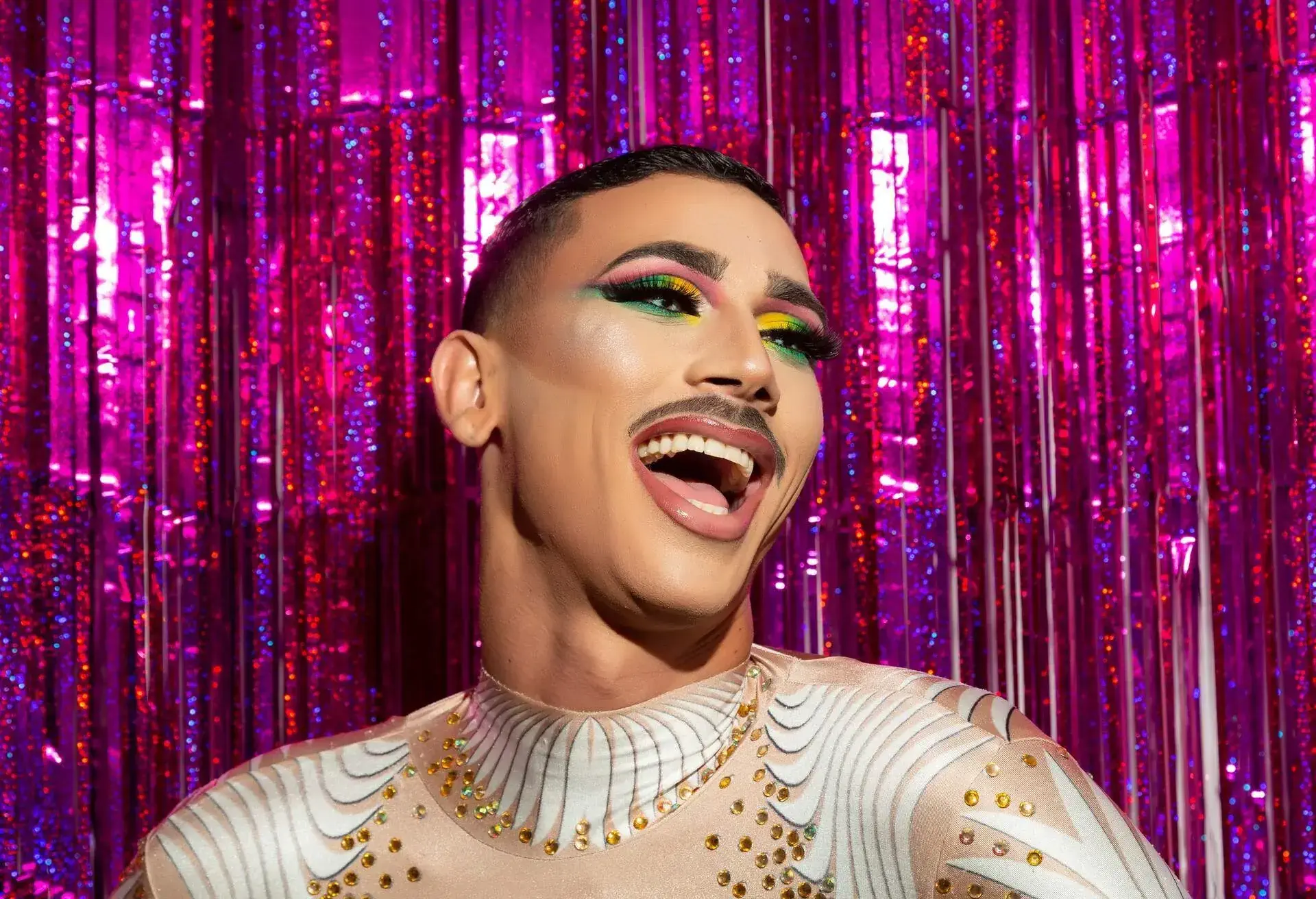 young gay man with makeup happy smiling with a colorful background 
