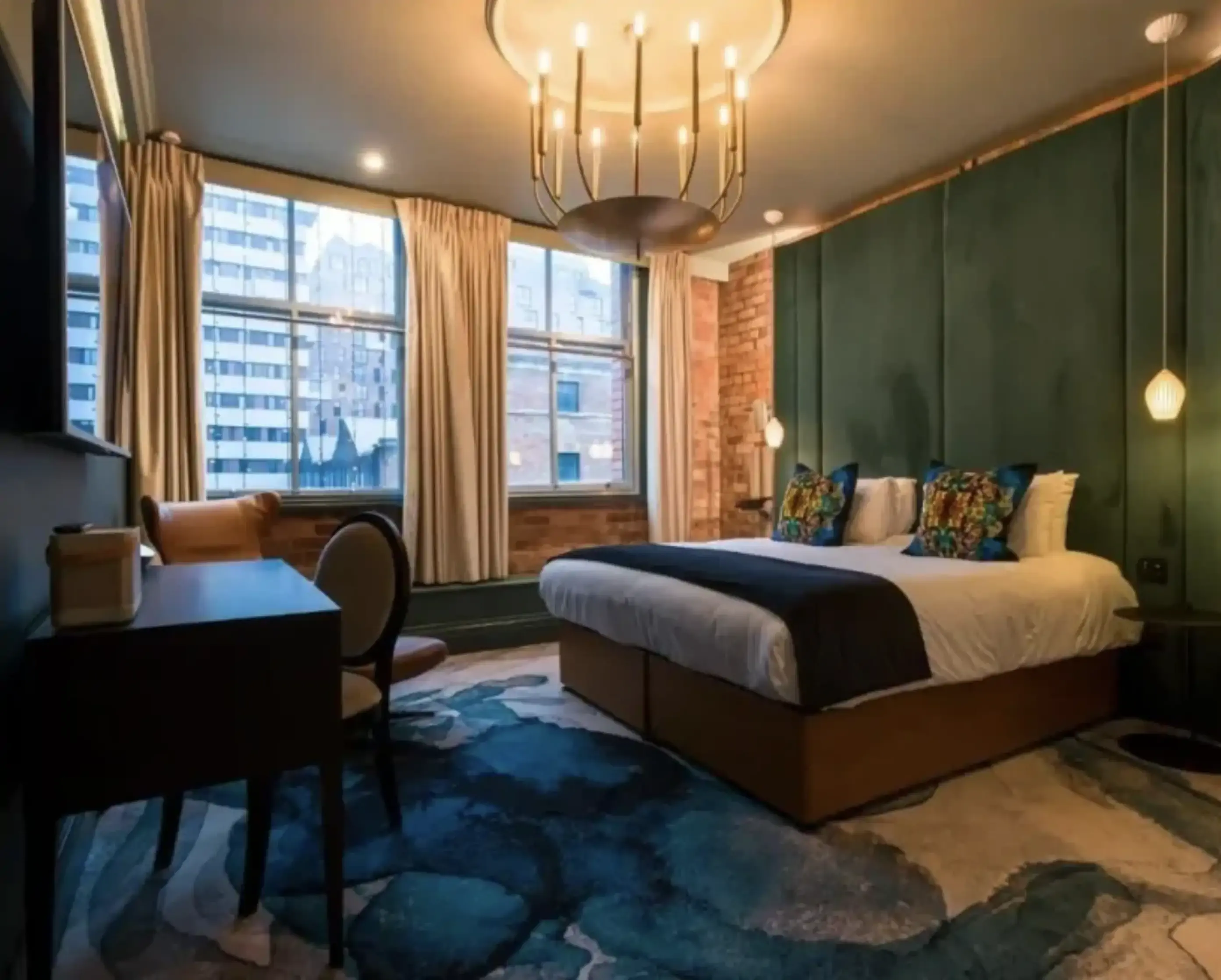 A luxurious hotel room featuring an emerald green accent wall, exposed brick, and a plush bed with colorful pillows.
