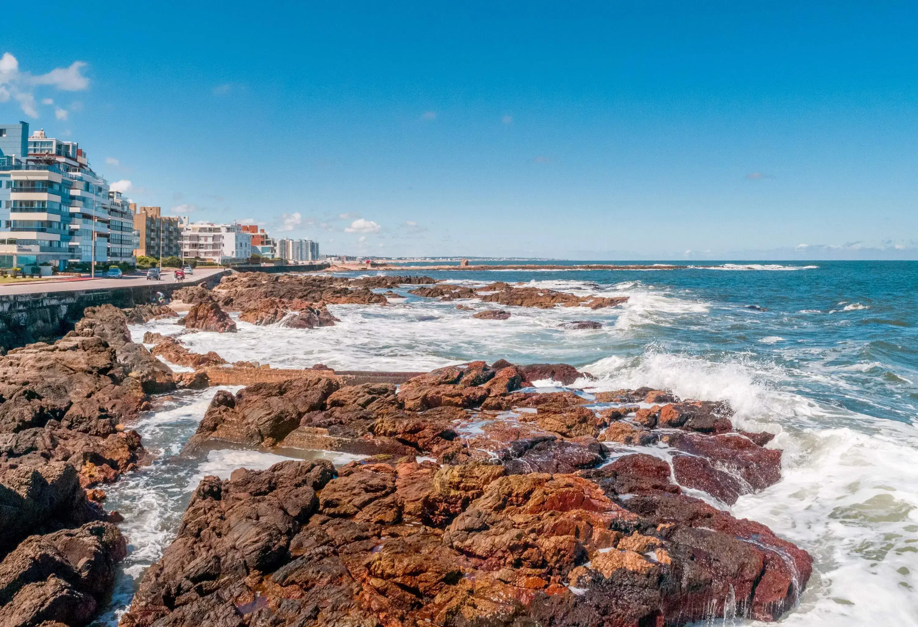 Rough waves smashing against the craggy shoreline of a large coastal city.