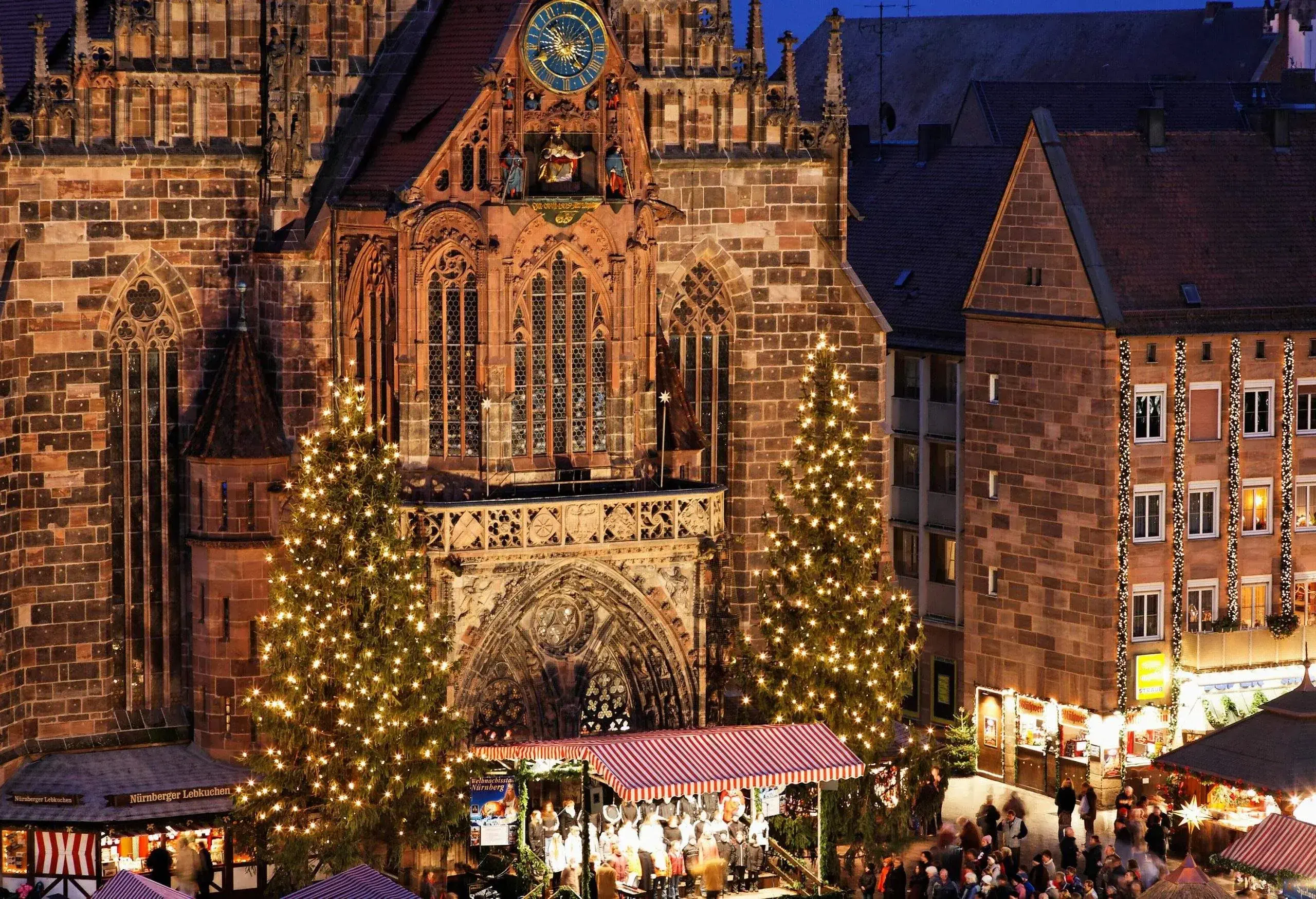 Une cathédrale en brique richement décorée de style gothique avec de grands arbres de Noël de chaque côté de son entrée et des boutiques de Noël sur la place principale.