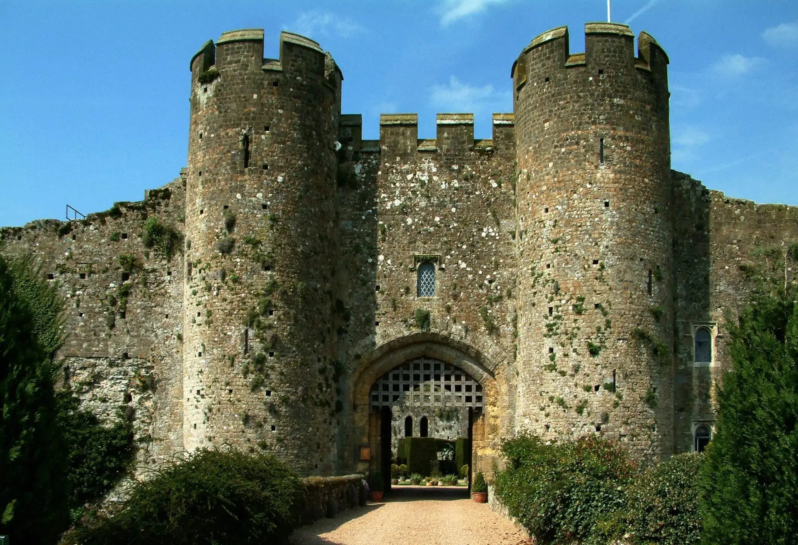An entryway to an old castle with a portcullis and two towers on either side, all surrounded by bushes. 