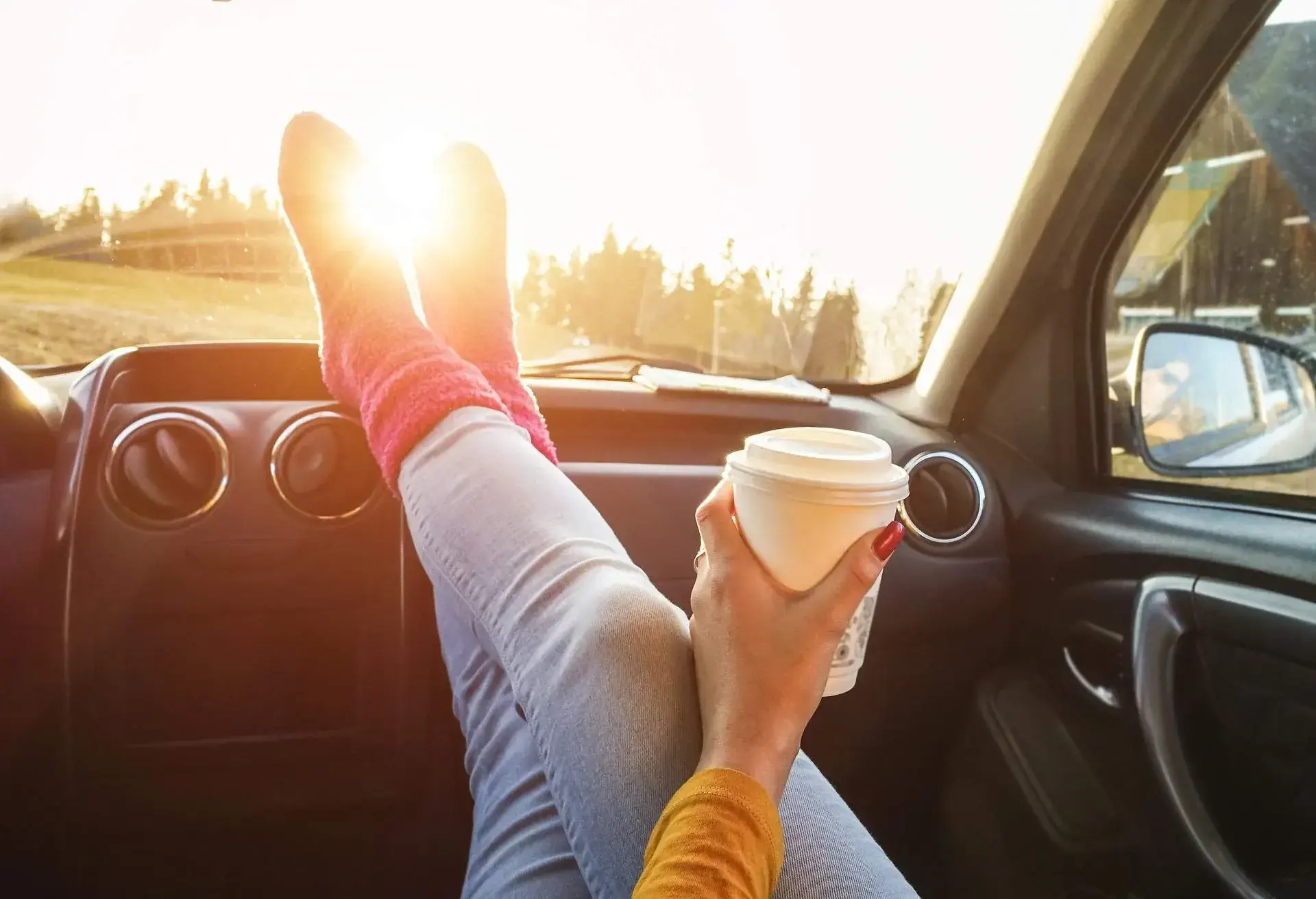 Woman putting her feet on the car dashboard while holding a cup of coffee