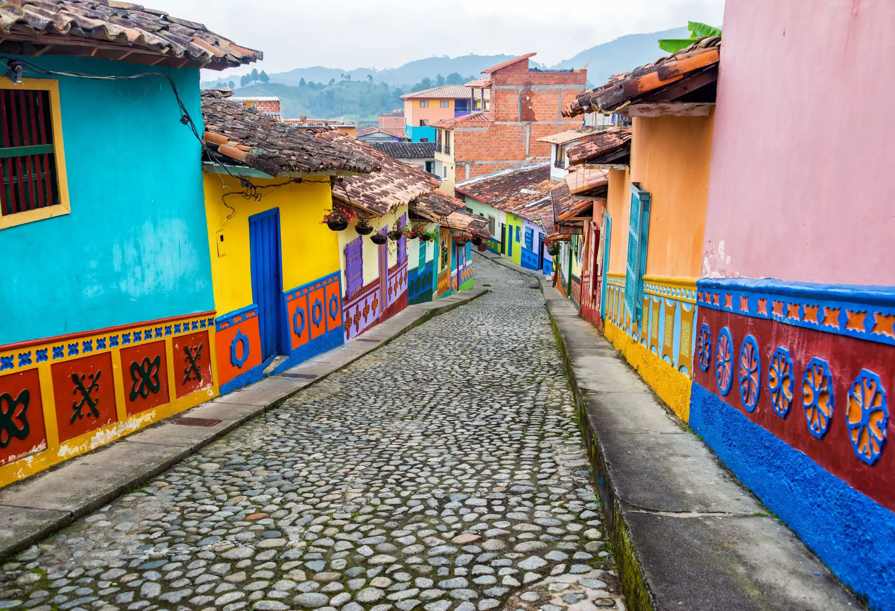A cobblestone street in a residential neighbourhood of colourful houses with tile roofs.