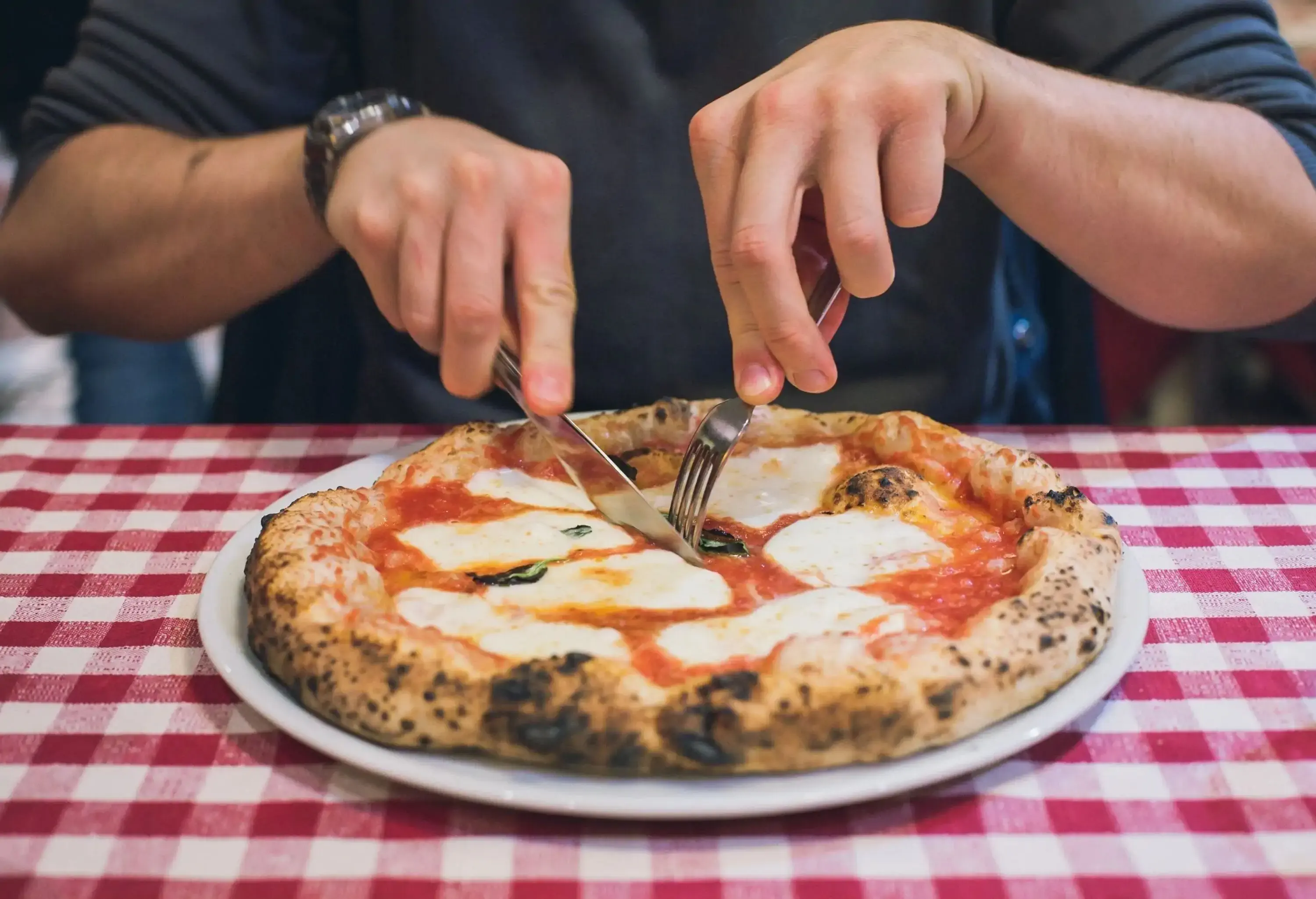 A man slicing a margherita pizza at a restaurant.