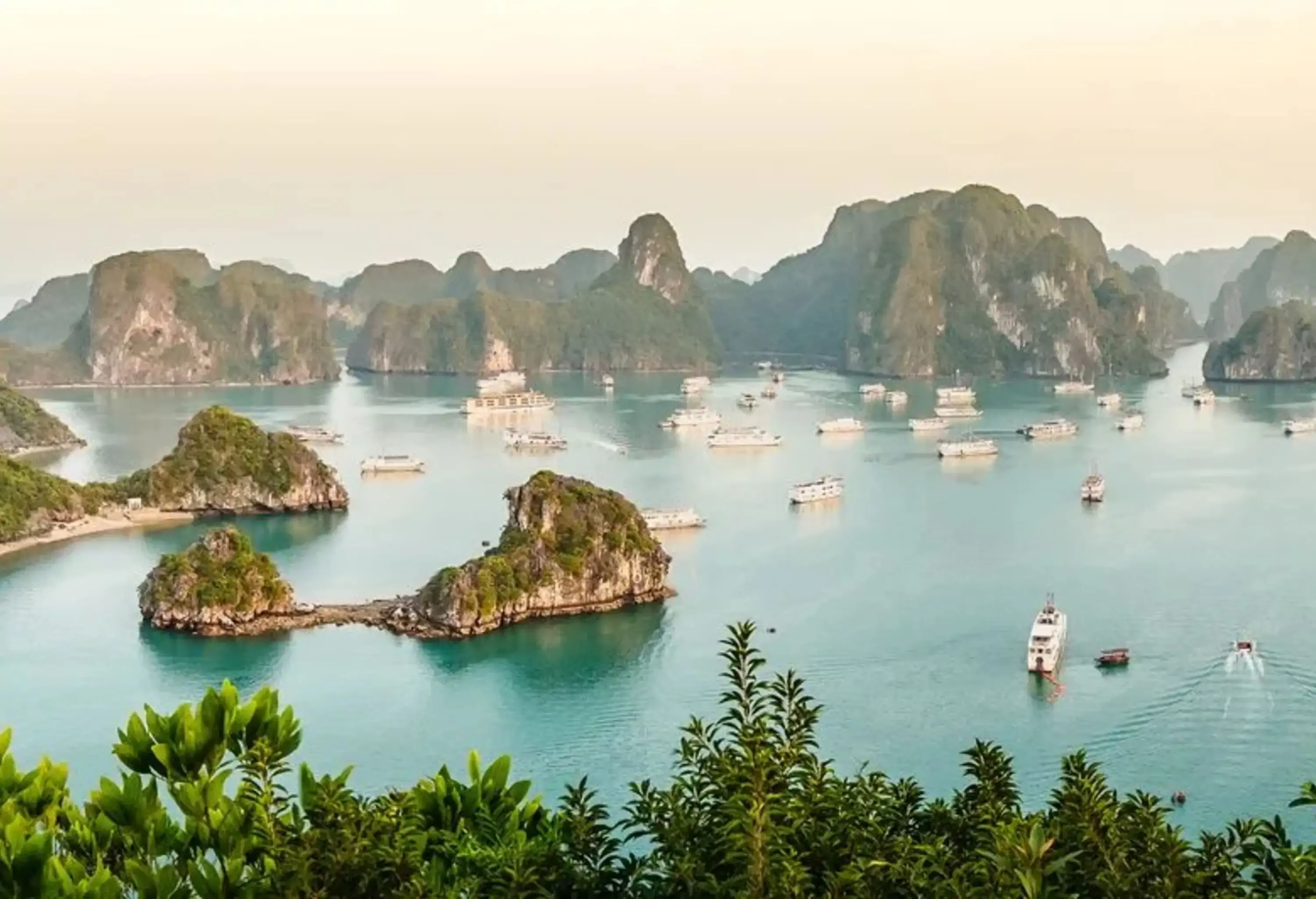 Panoramic view of wonderful towering rock limestone islands topped by rainforests, surrounded by the majestic turquoise sea dotted with cruise ships, captured during the early morning.
