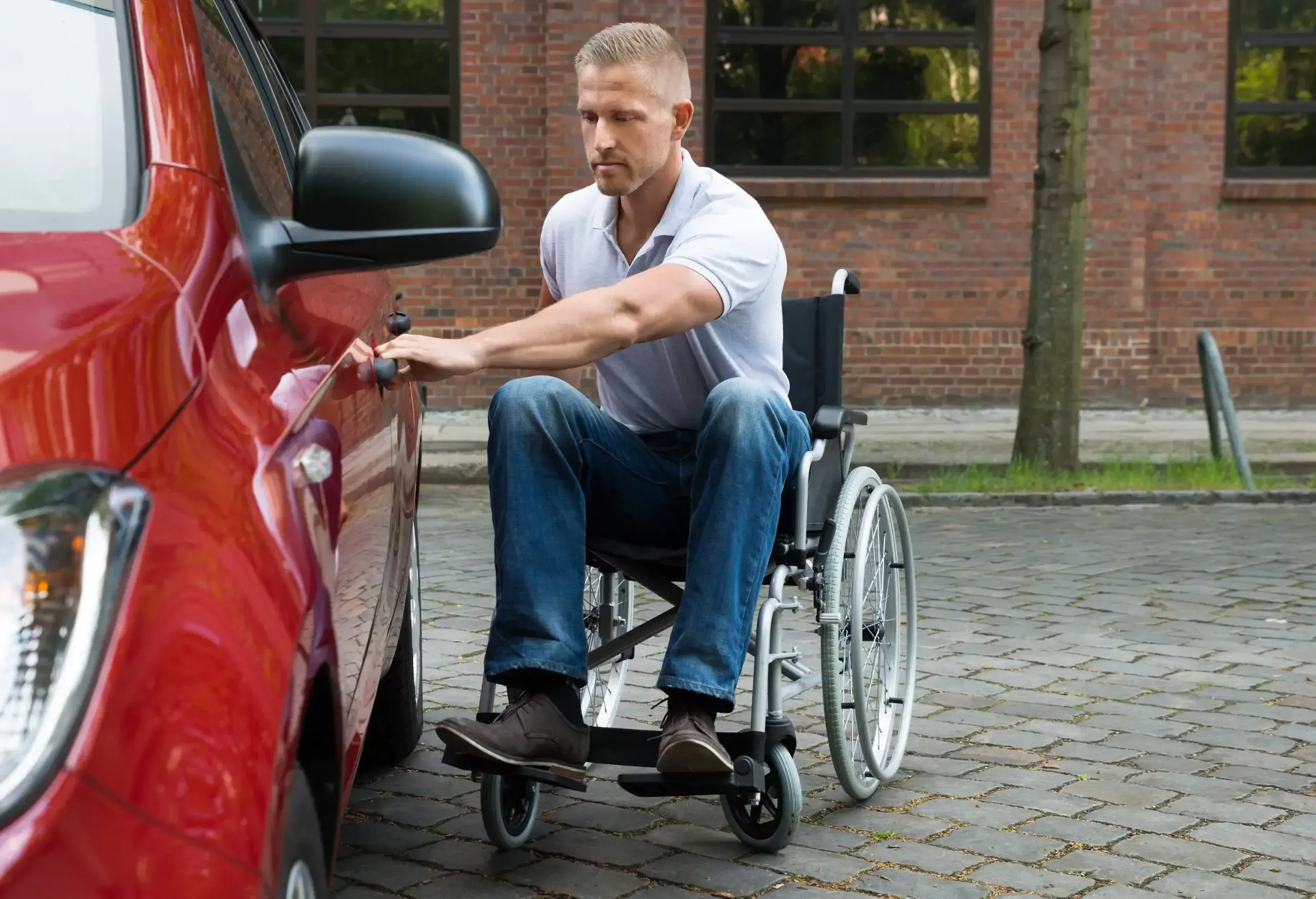 A man in a wheelchair opening the door of a red car