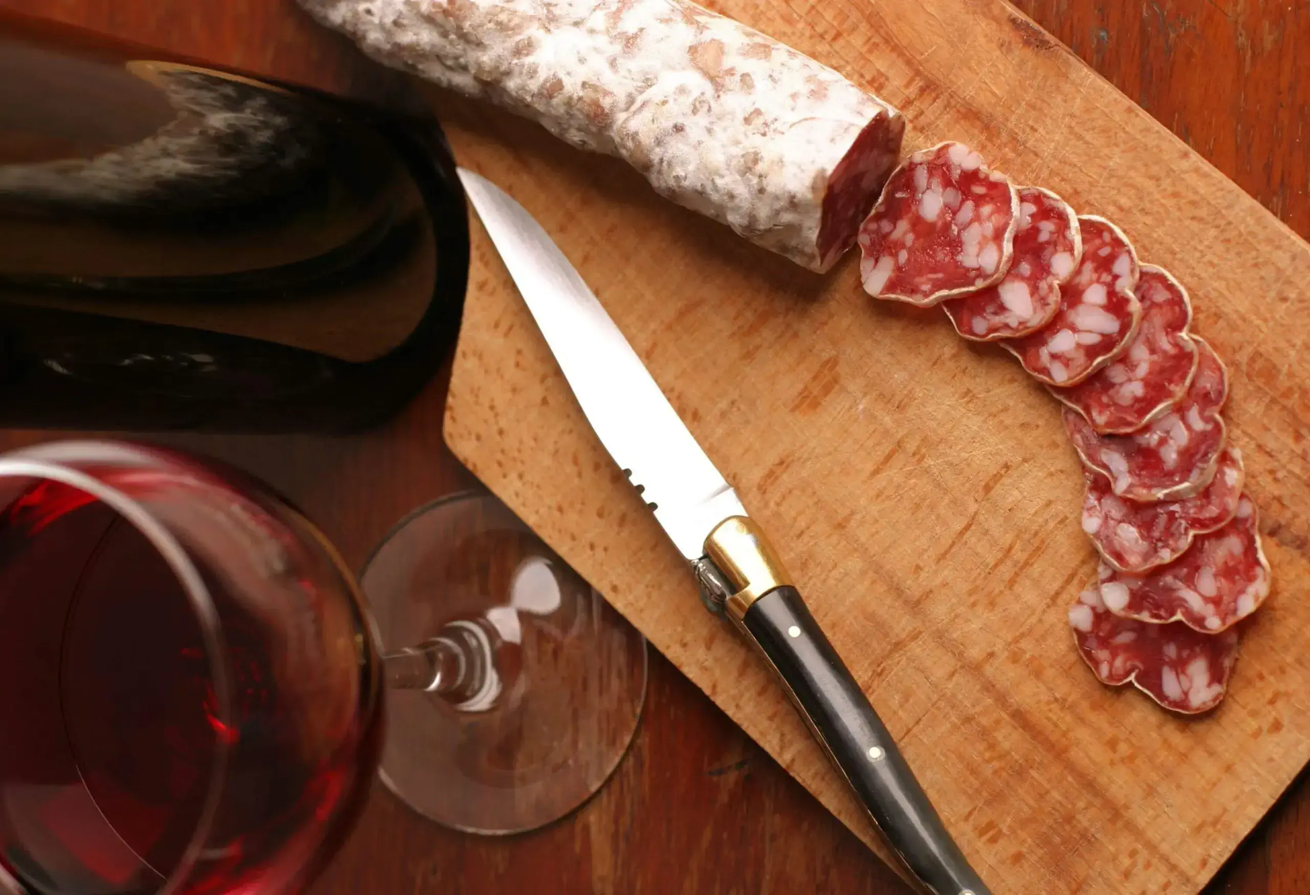 A glass of red wine, a Laguiole knife and a dry sausage on a chopping board