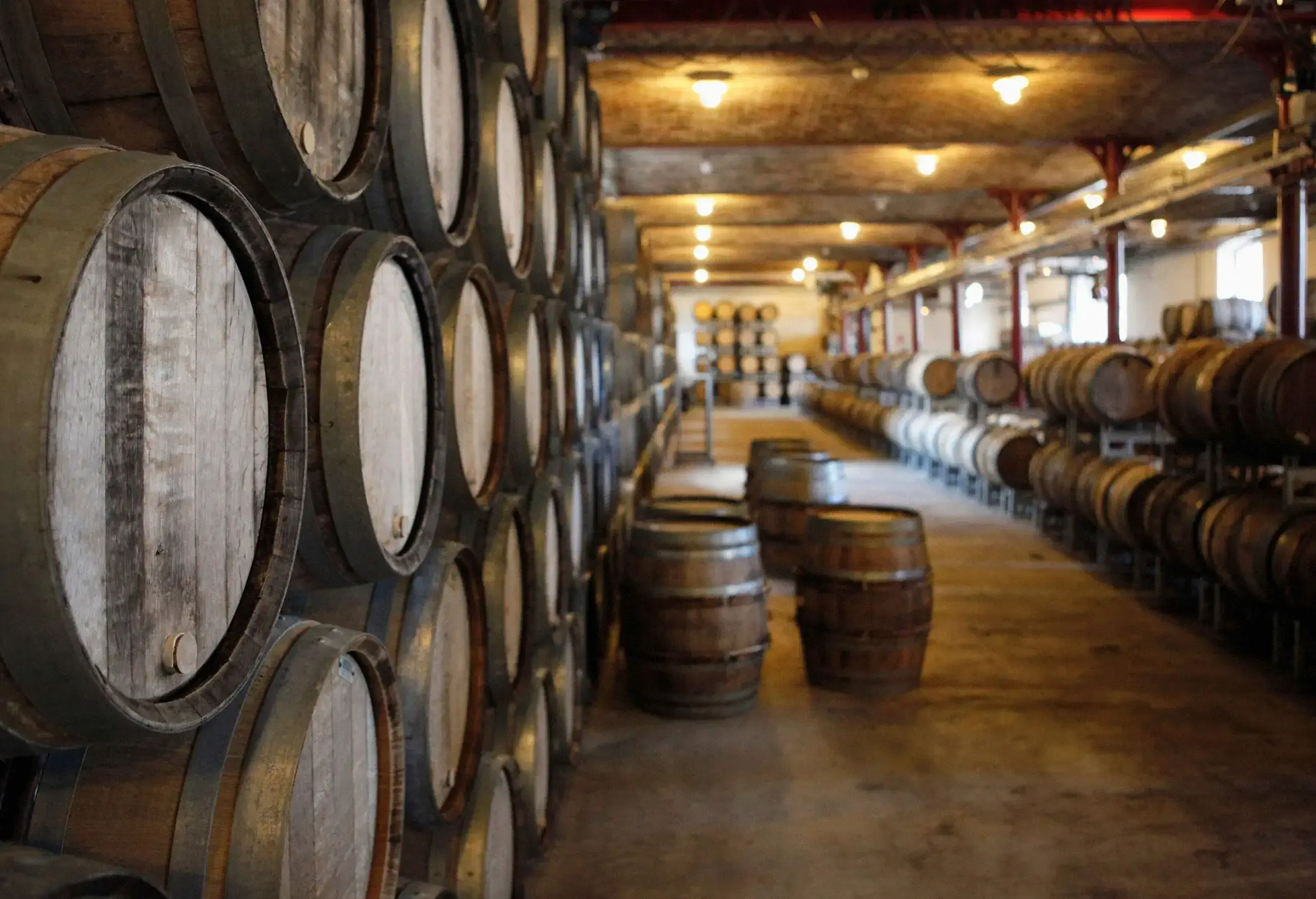 In a wine cellar, brown wine barrels are stacked on both sides, with some on the aisle.