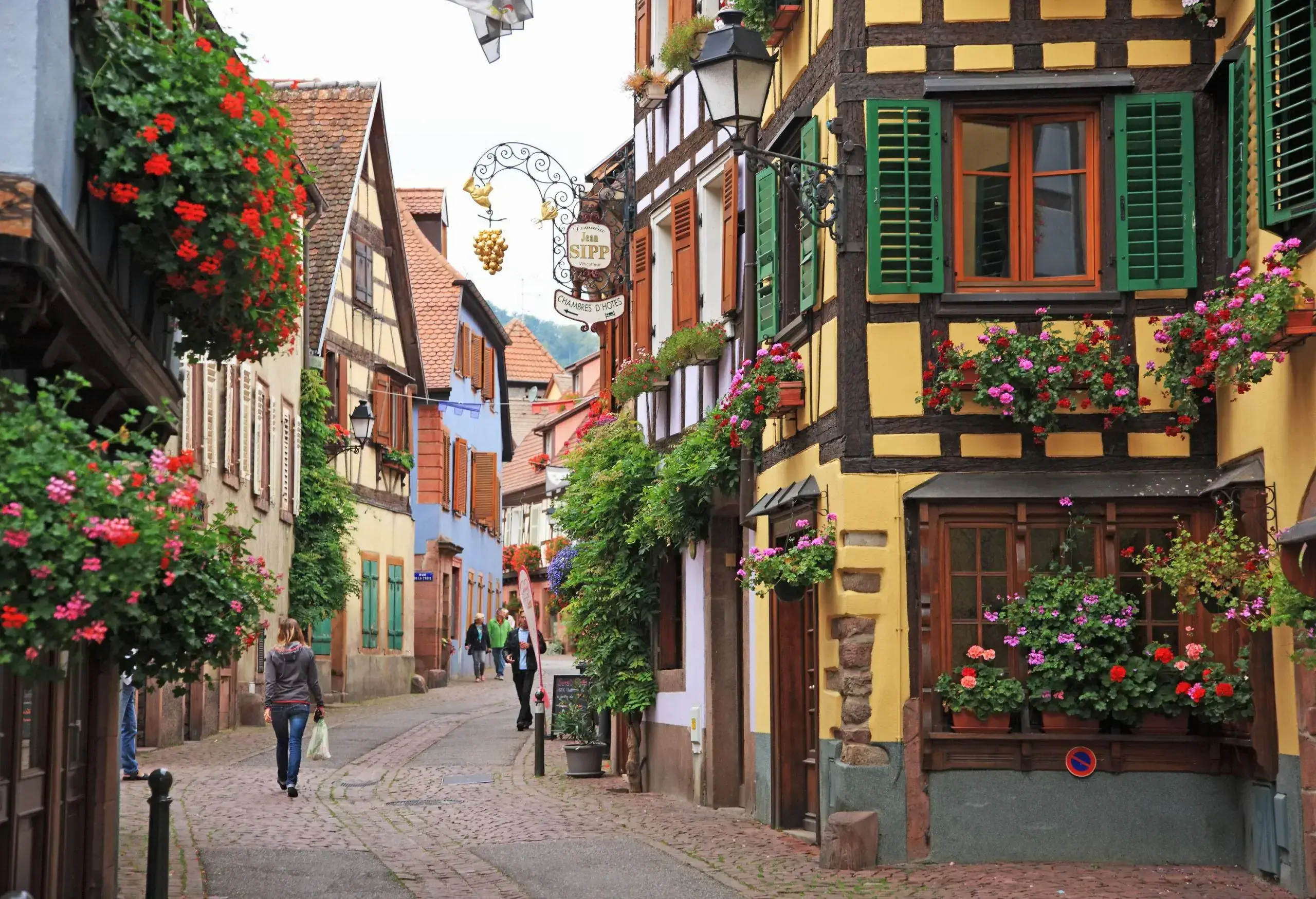 People walk in a cobbled alleyway in the middle of colourful houses.