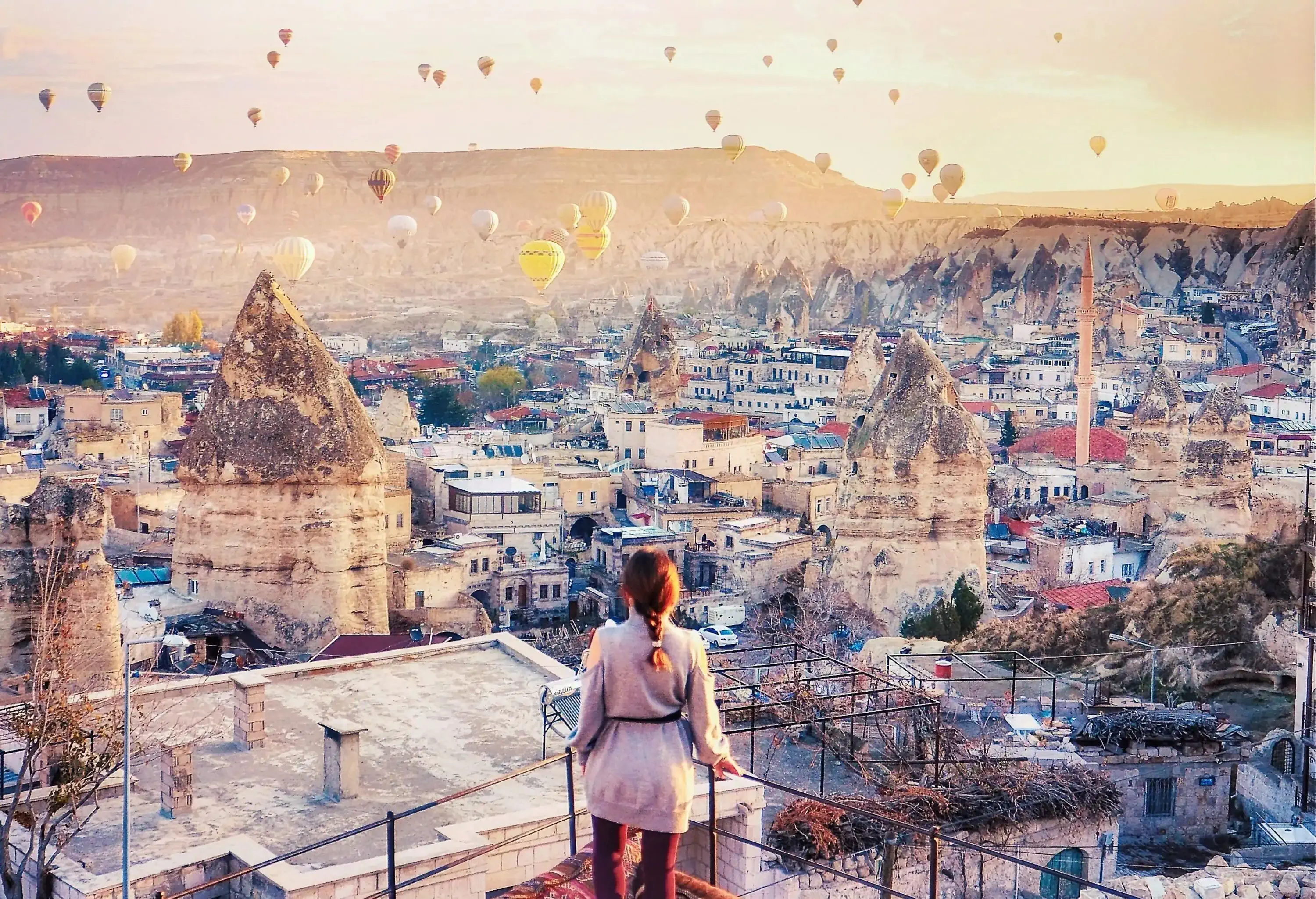 Beautiful women stand at hotel rooftop watching hot air balloons flying over city Ürgüp Cappadocia, Turkey