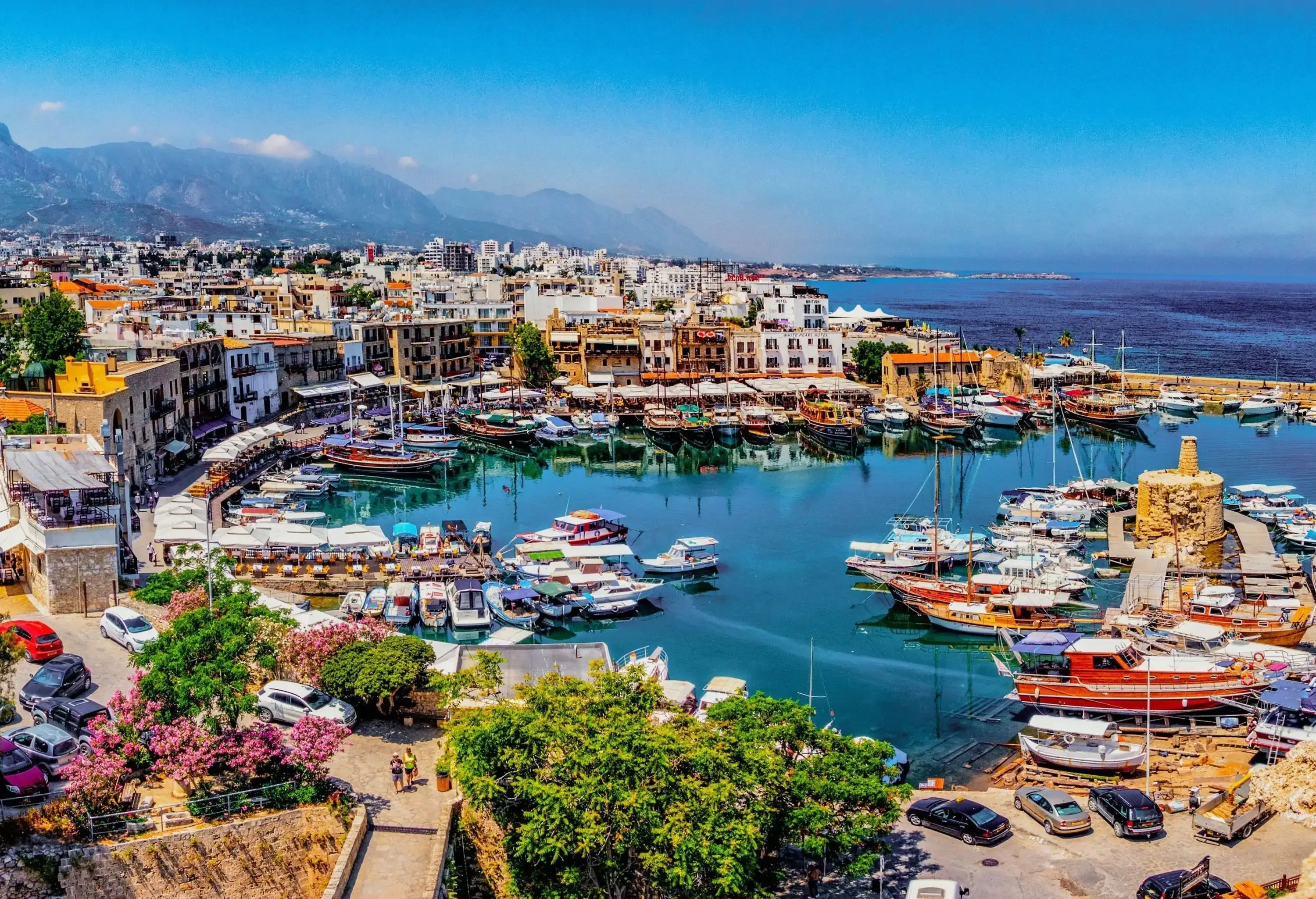 A harbour town with a pier that wraps around a marina and colourful buildings along the shore.