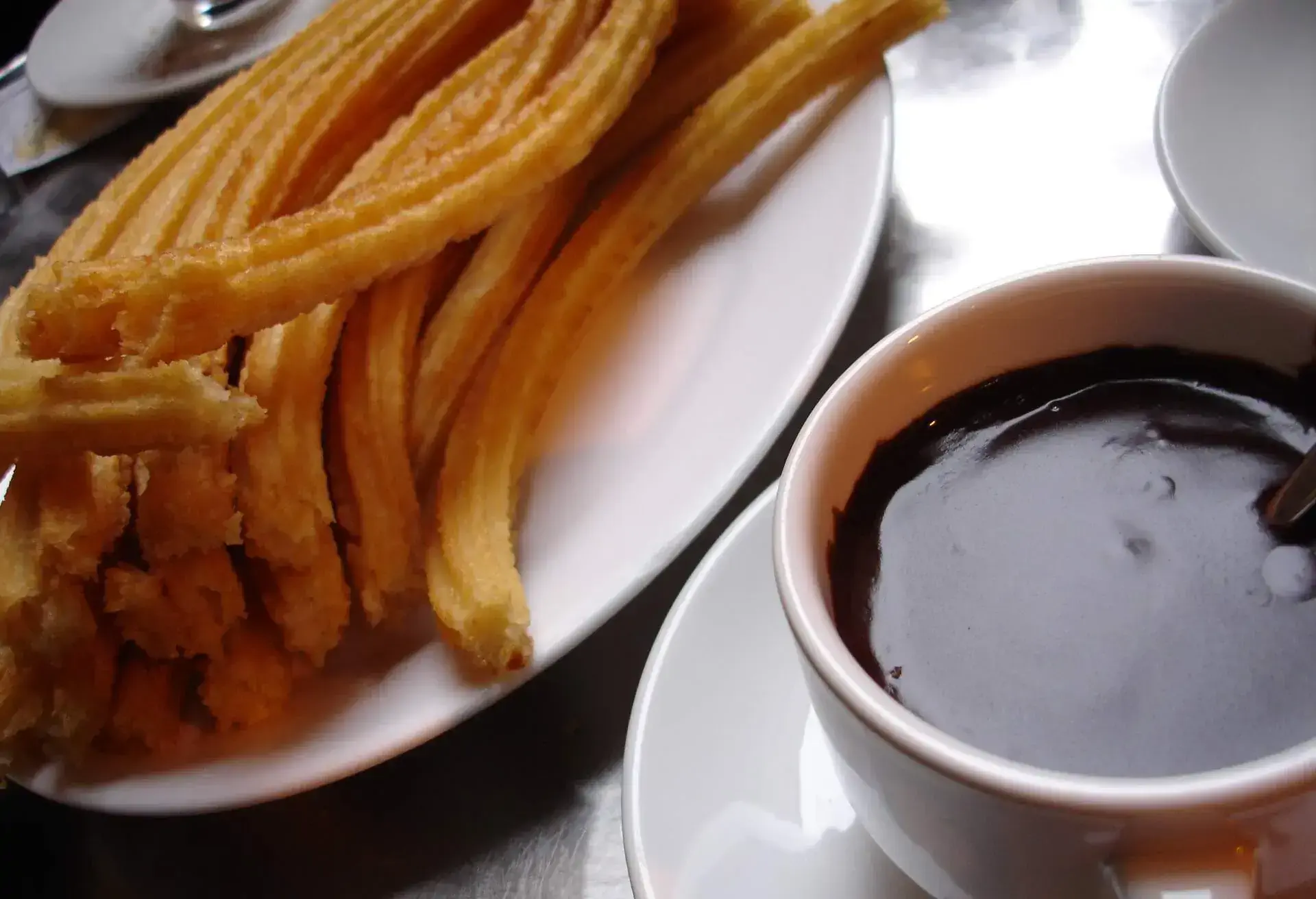 Churros on a white plate with a cup of dipping chocolate