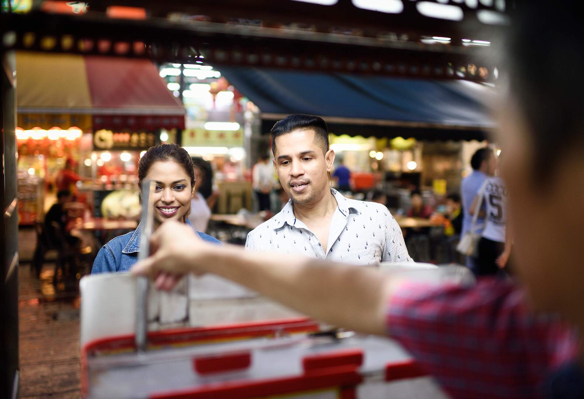A lovely young couple interacting with a male vendor in a shopping street.