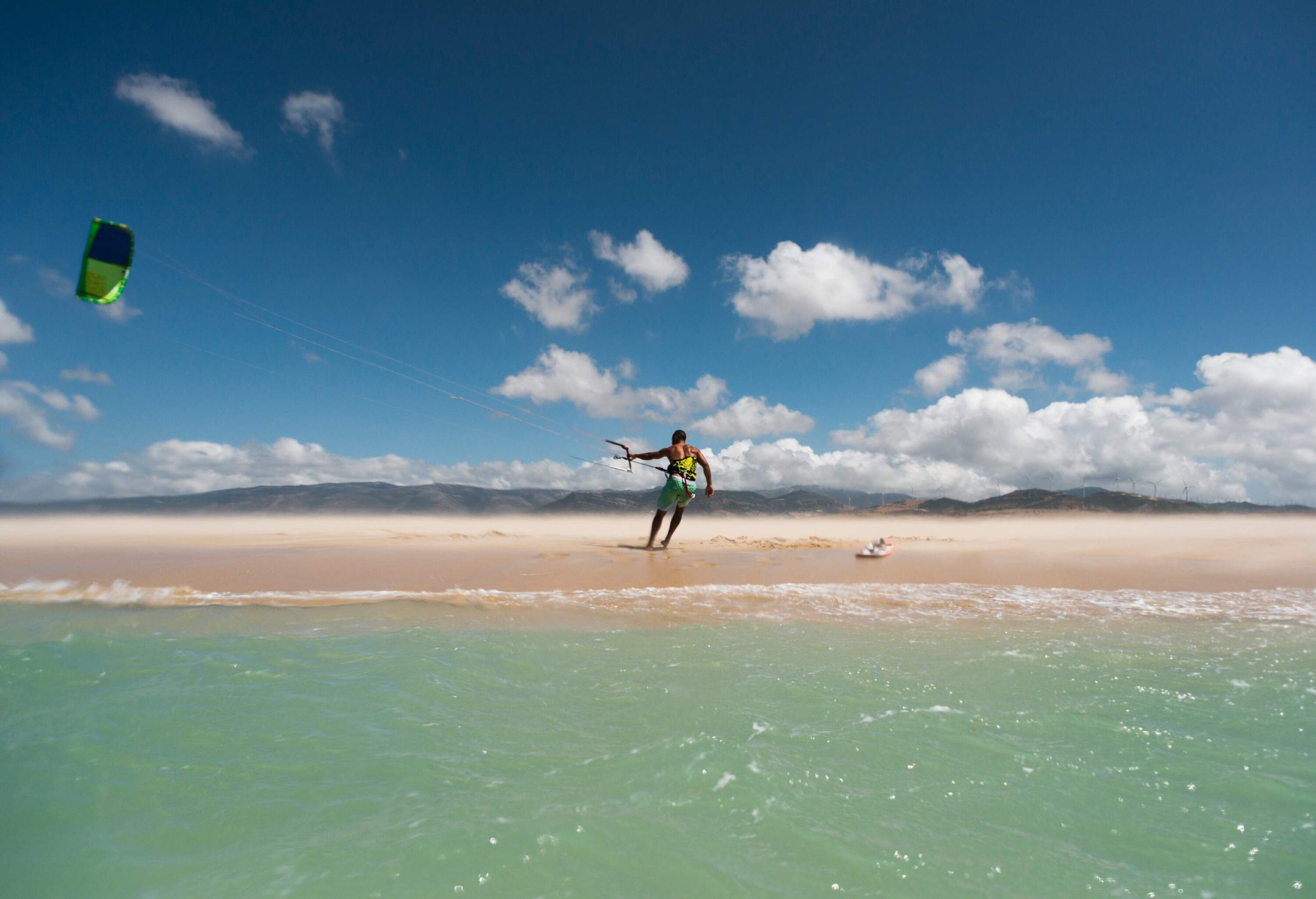 A person harnessed in a green paraglider on the shore of the beach. 