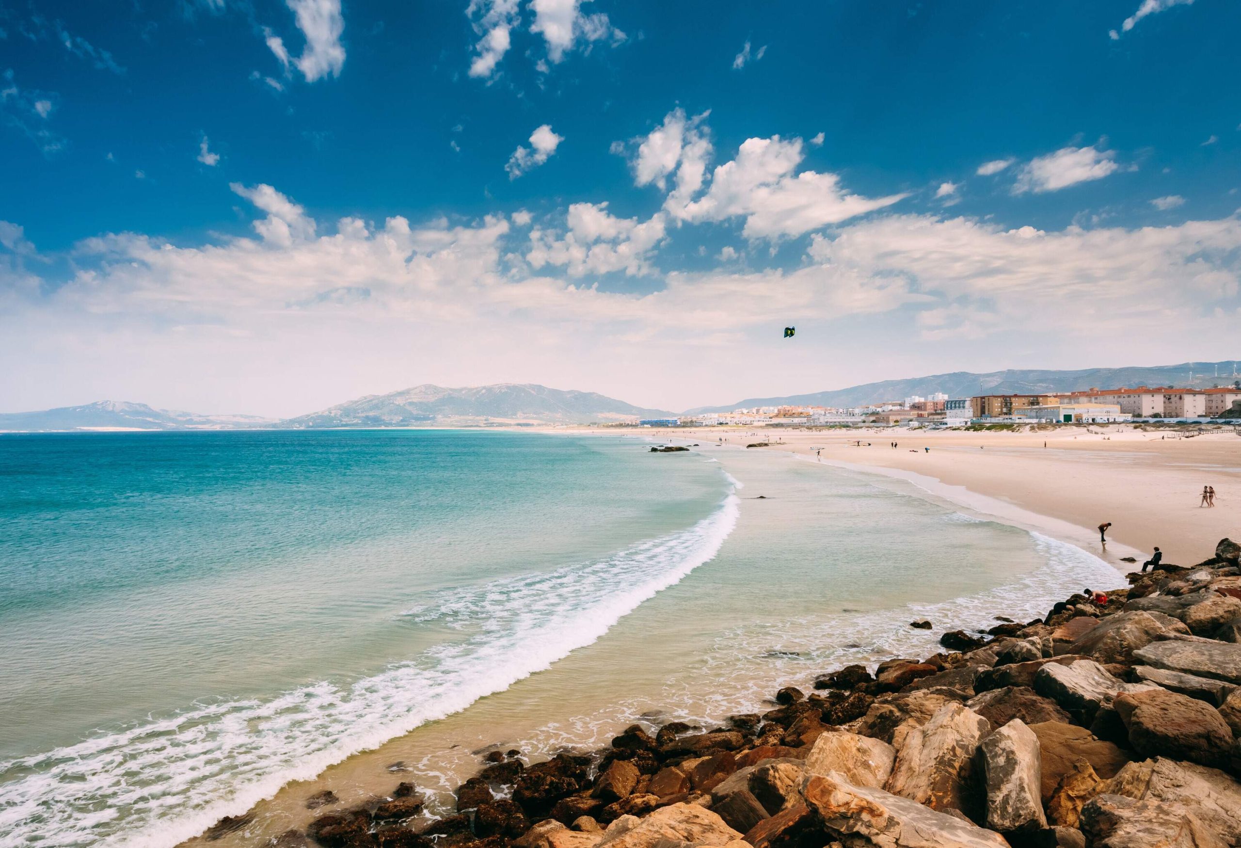 Tranquil blue water beach with a white sandy shore against the cloudy blue sky.