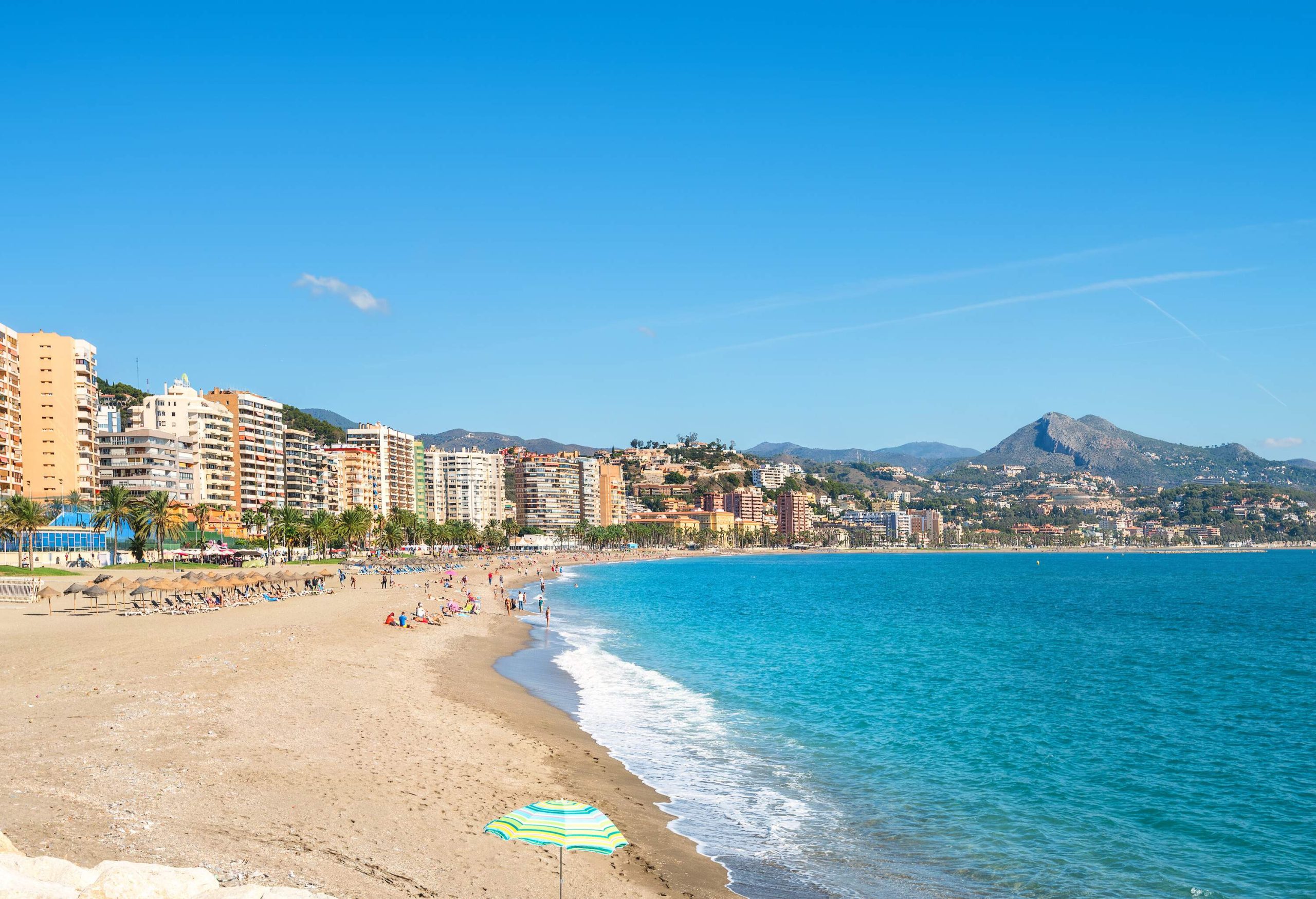 A crowded beach with views of high-rise buildings along the coast.