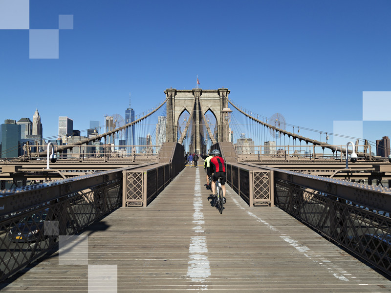 Brooklyn Bridge with New York City in the background and tourists in the foreground on a blue sky day
