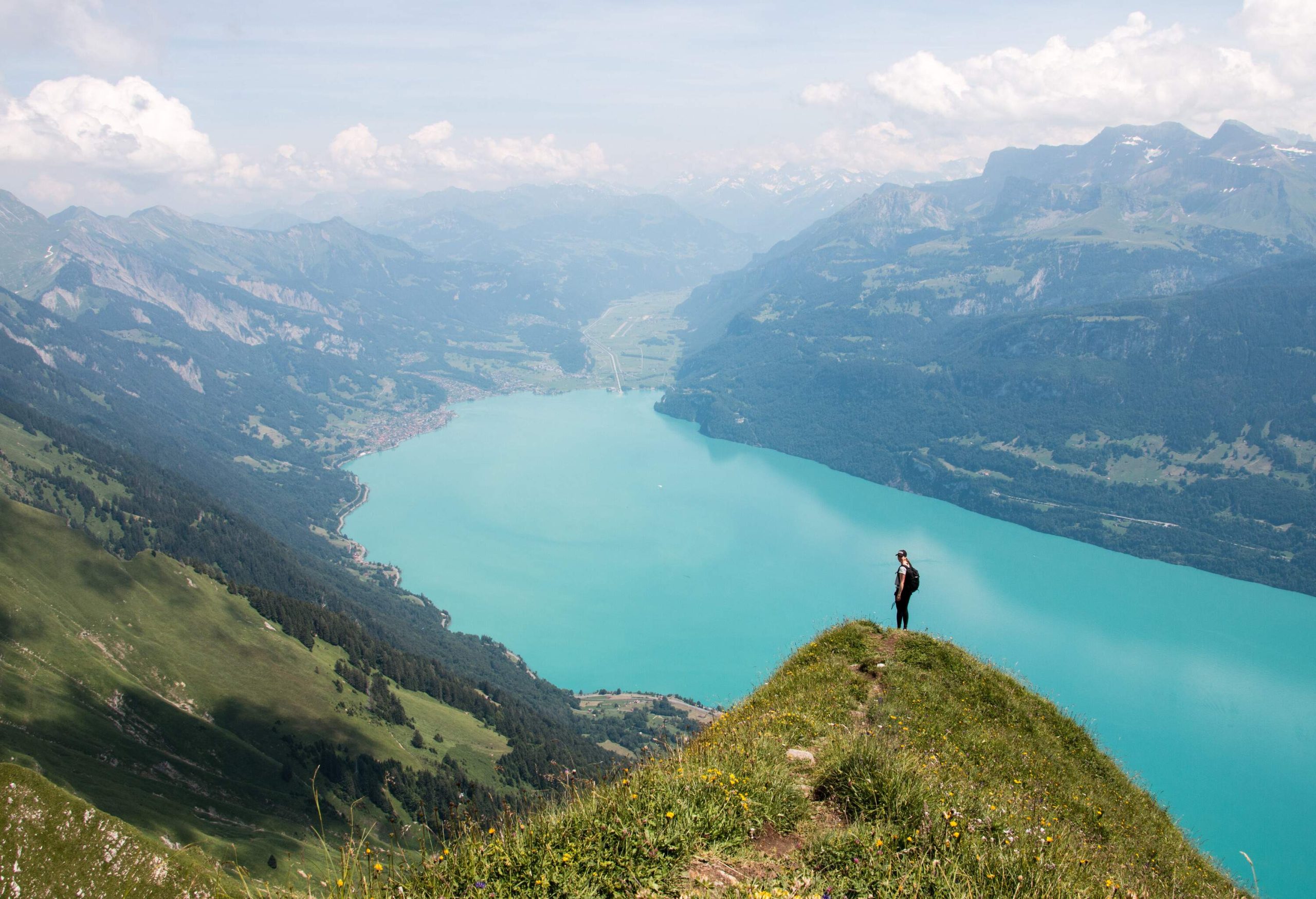 A female hiker standing on a mountaintop with epic views of a blue lake and mountain ranges.