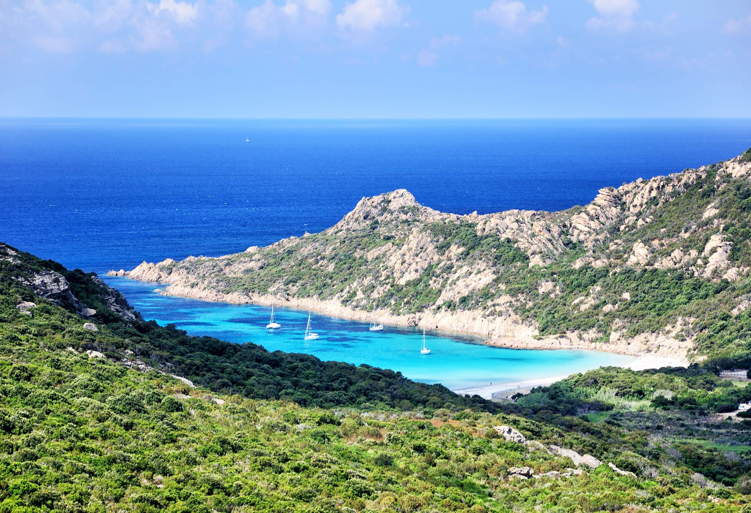 A bay with cruising sailboats bordered by rugged hills.