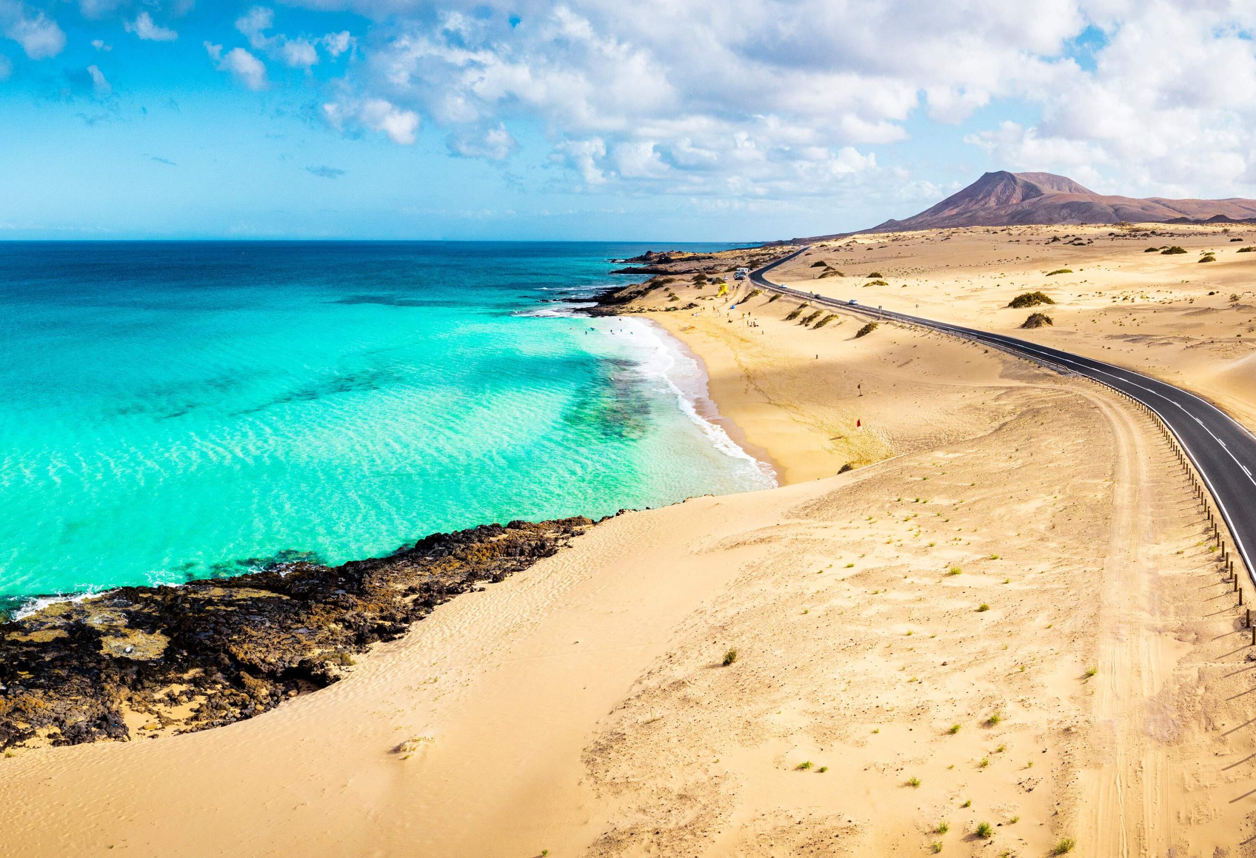 A white car on the road along the sandy beaches of a turquoise sea.