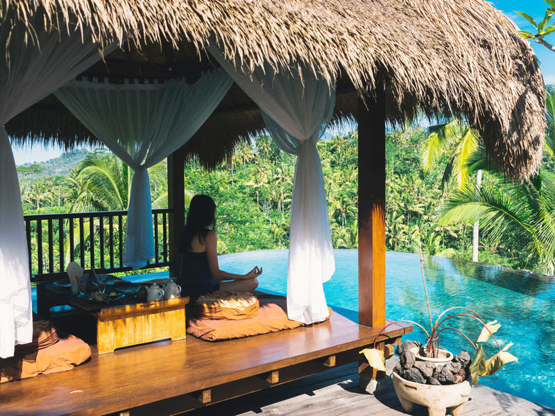 Une femme médite sur une terrase ombragée à Bali au bord d'une piscine à débordement