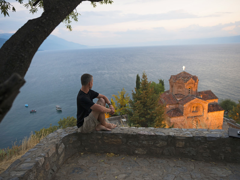 un homme contemple le lac d'Ohrid en Macédoine au bord duquel se trouve une belle église ancienne