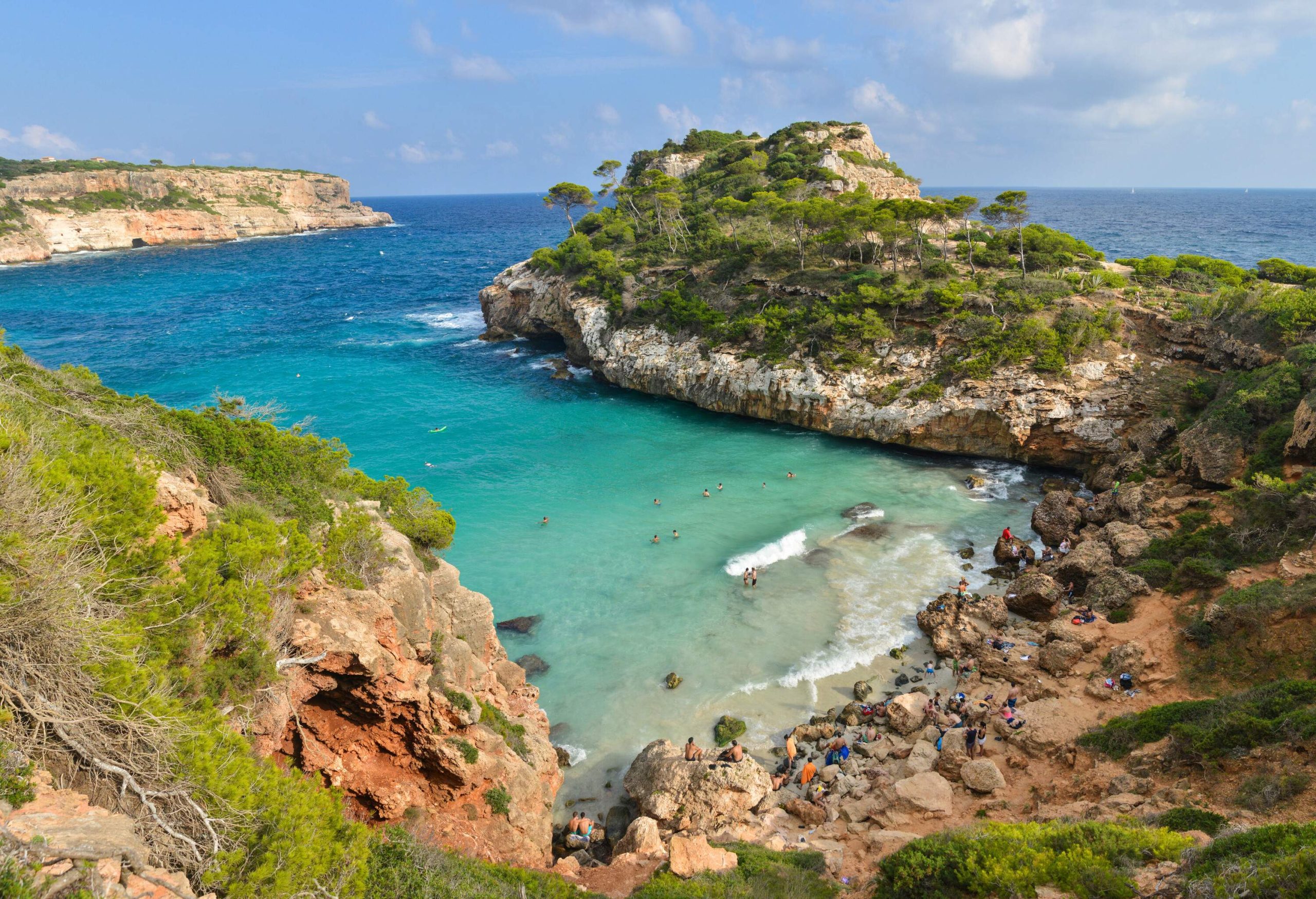 A beach with clear turquoise waters surrounded by trees on top of sheer cliffs.