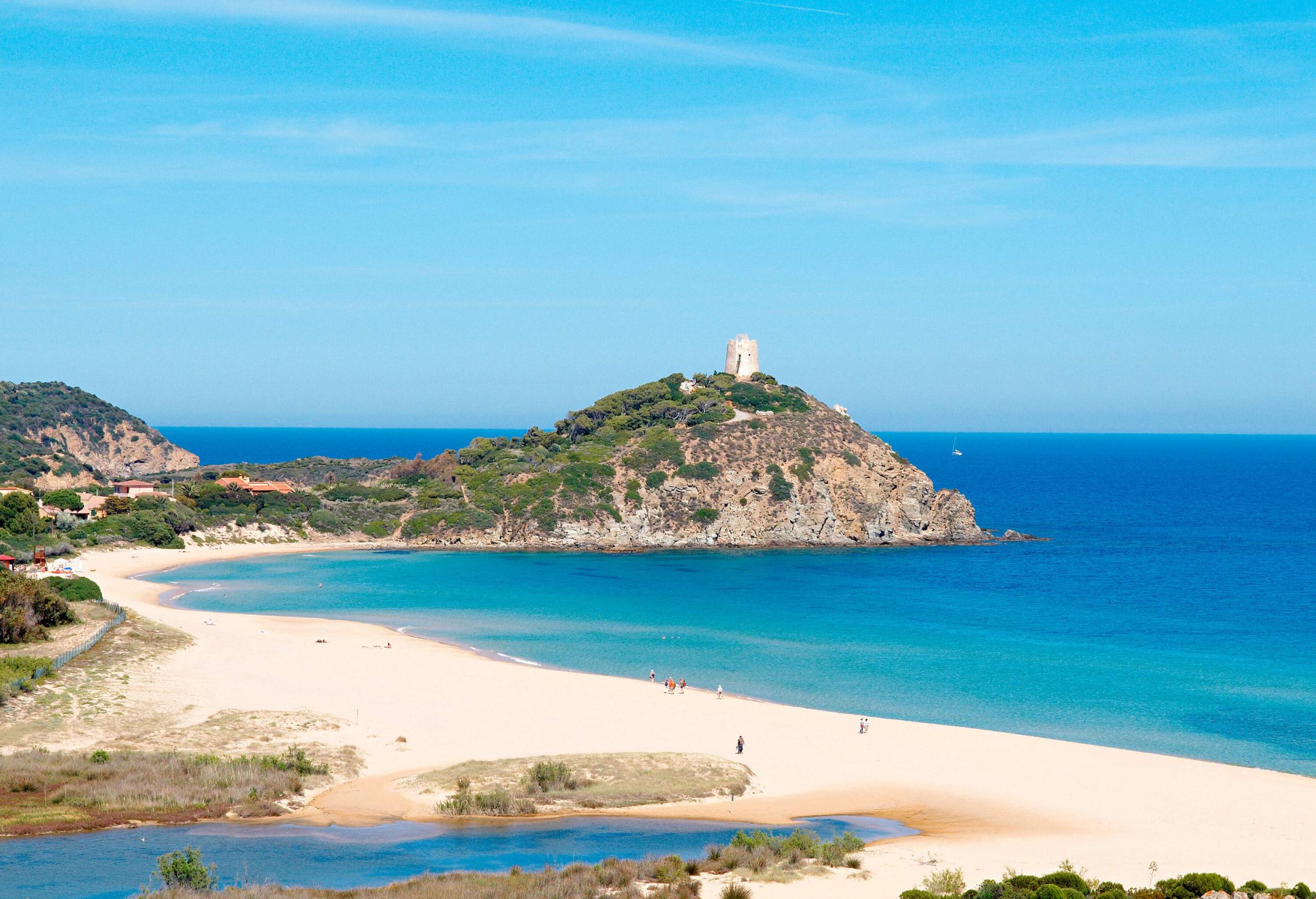 High angle view of white sand beach surrounded by turqoise blue water with mountain and medieval tower in the background