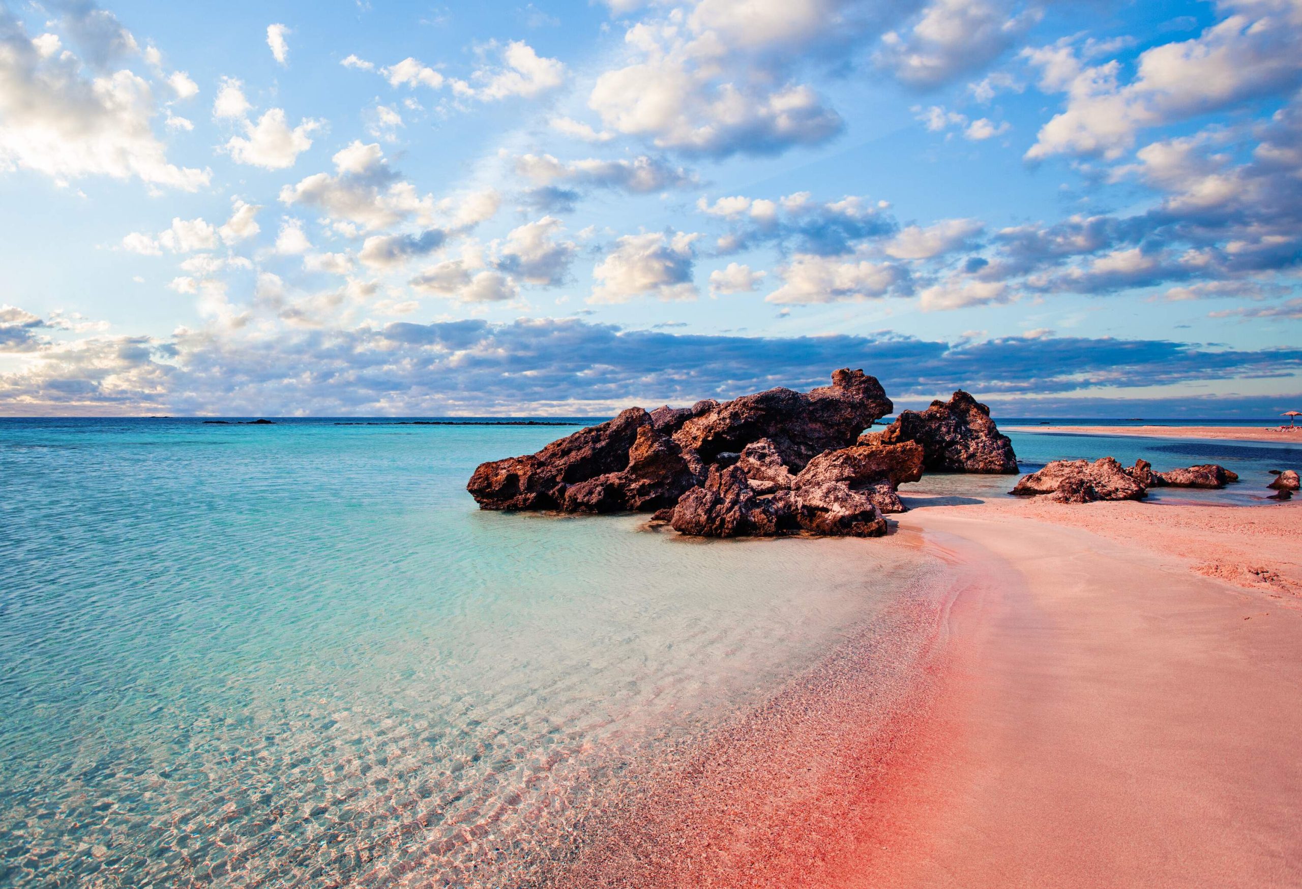 A pink sand beach with turquoise waters and rugged boulders on the shore.