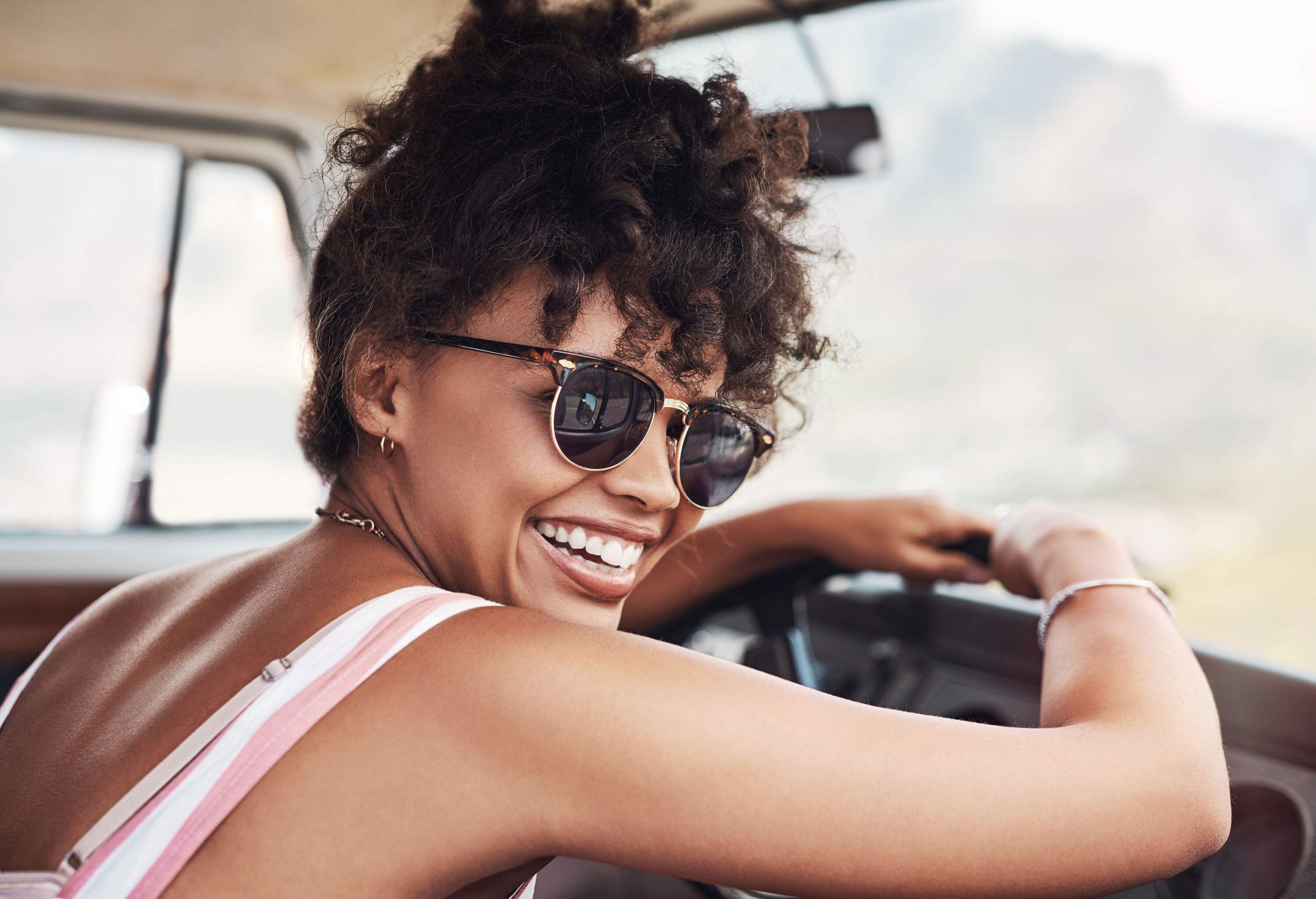 A woman with a beautiful smile leaning against the steering wheel of her car.