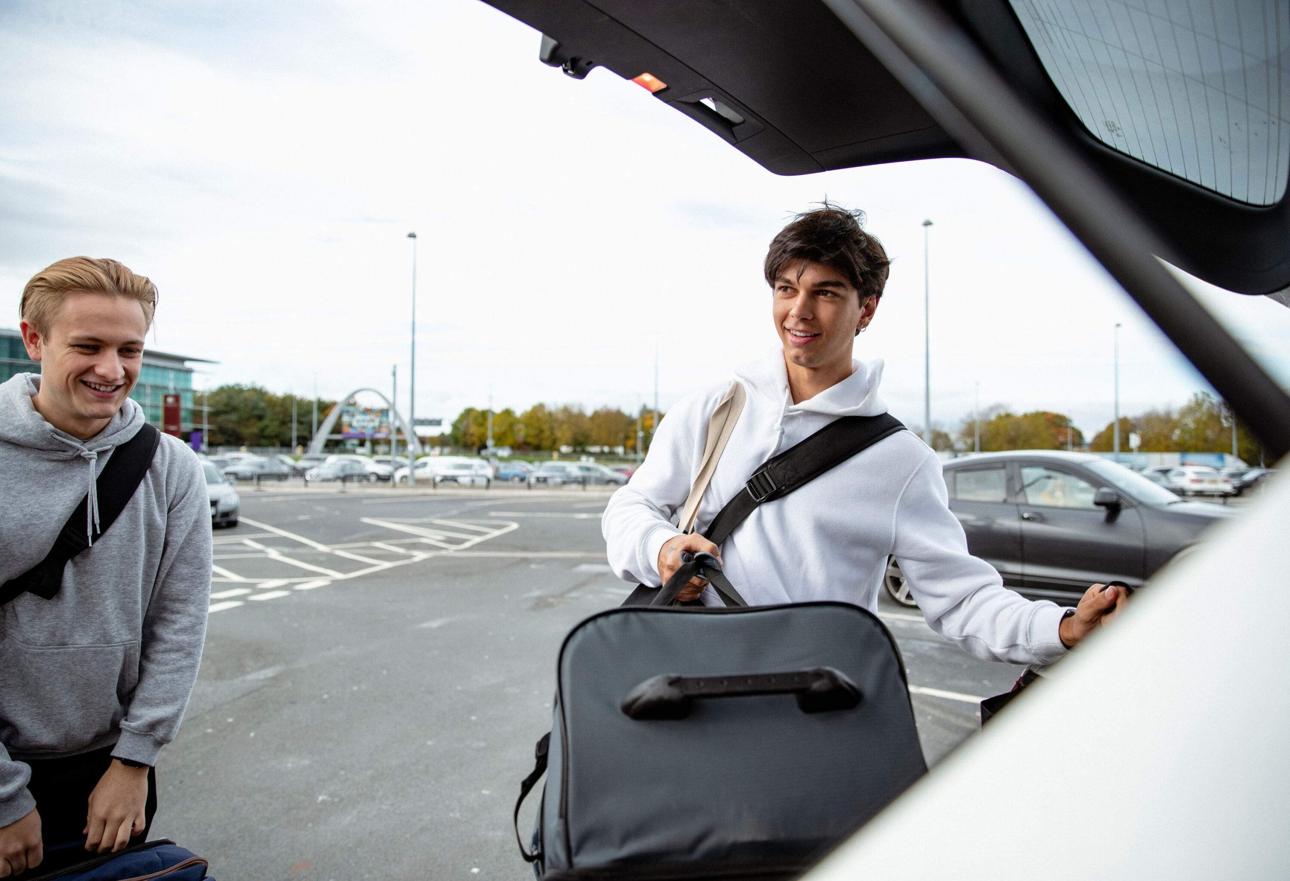 Two young men taking luggage out of a car trunk, ready to go on holiday.