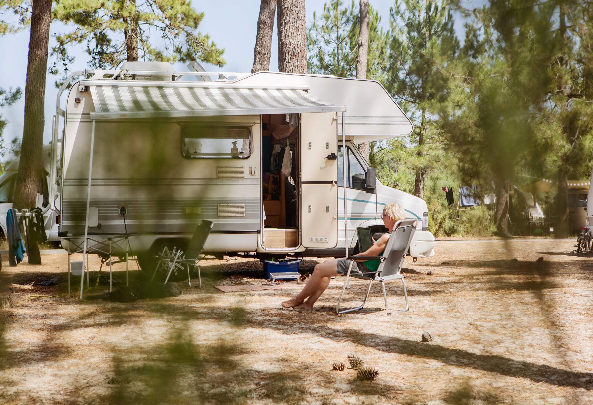 A woman using a tablet while sitting on a folding chair next to a motorhome.