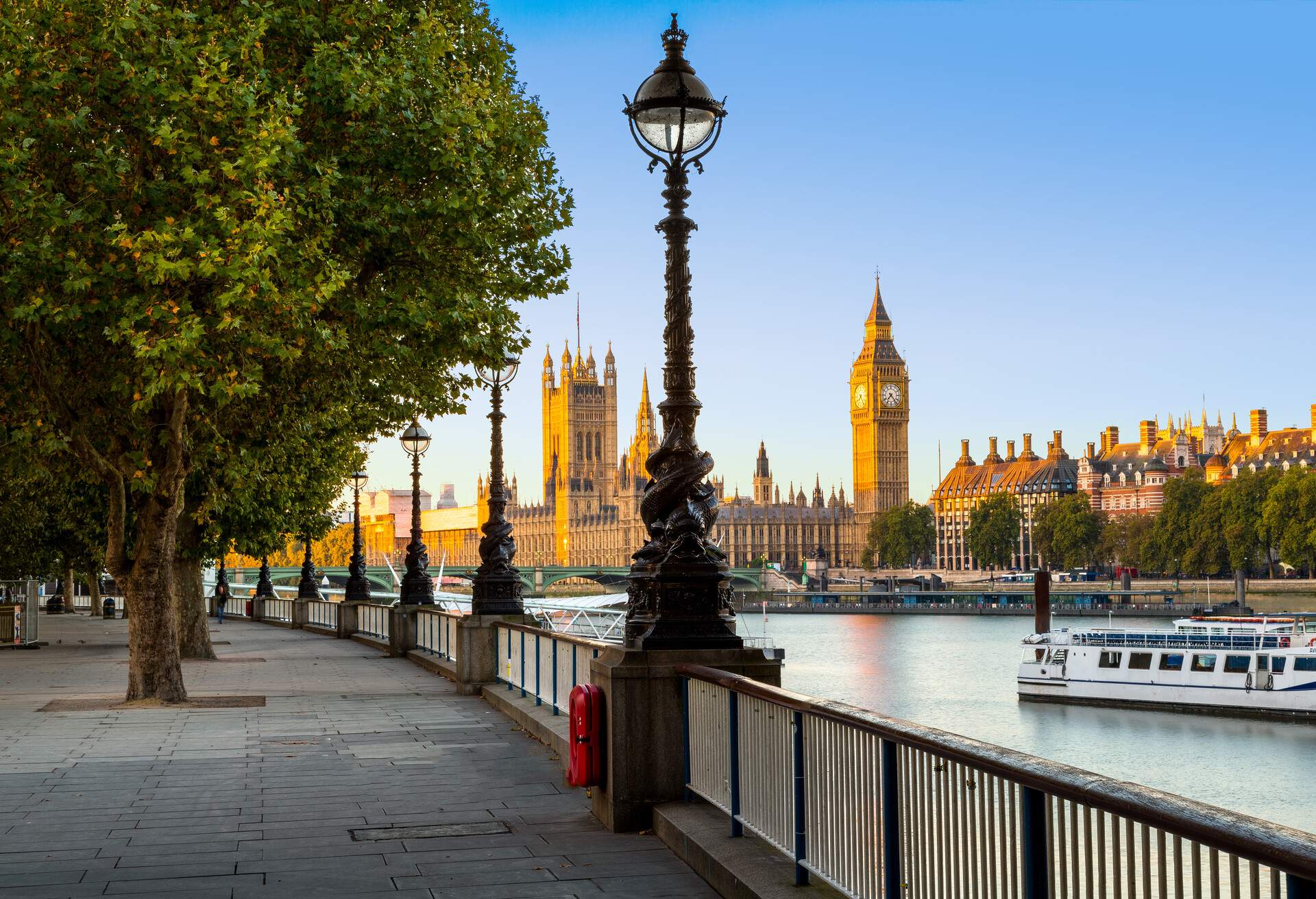 A tree-lined promenade along the River Thames, with the Big Ben in the backdrop.