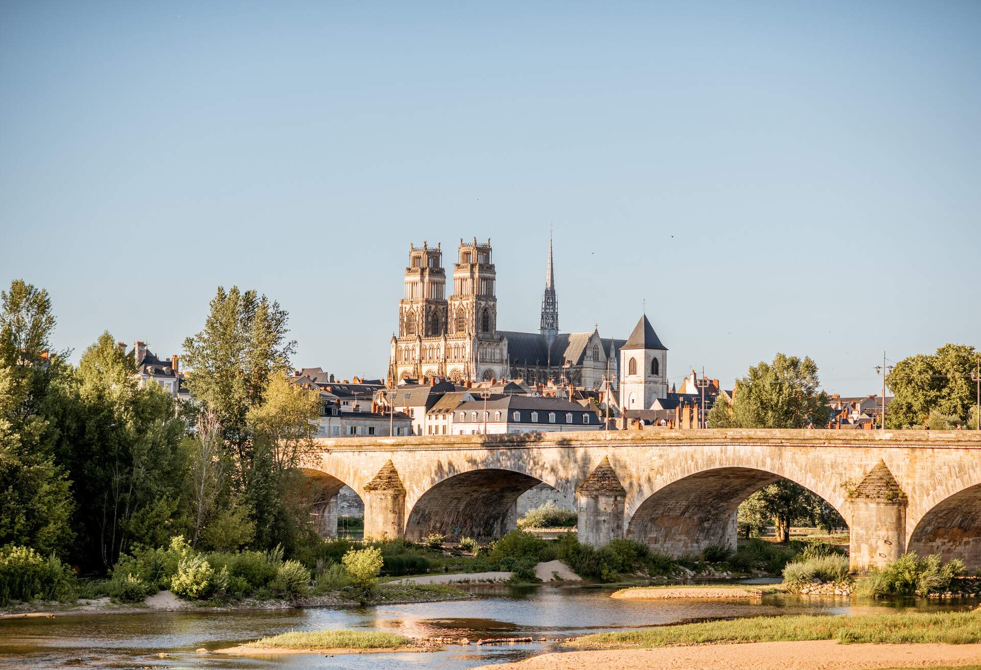 An old arch bridge across a river surrounded by trees with a view of a church in the background.