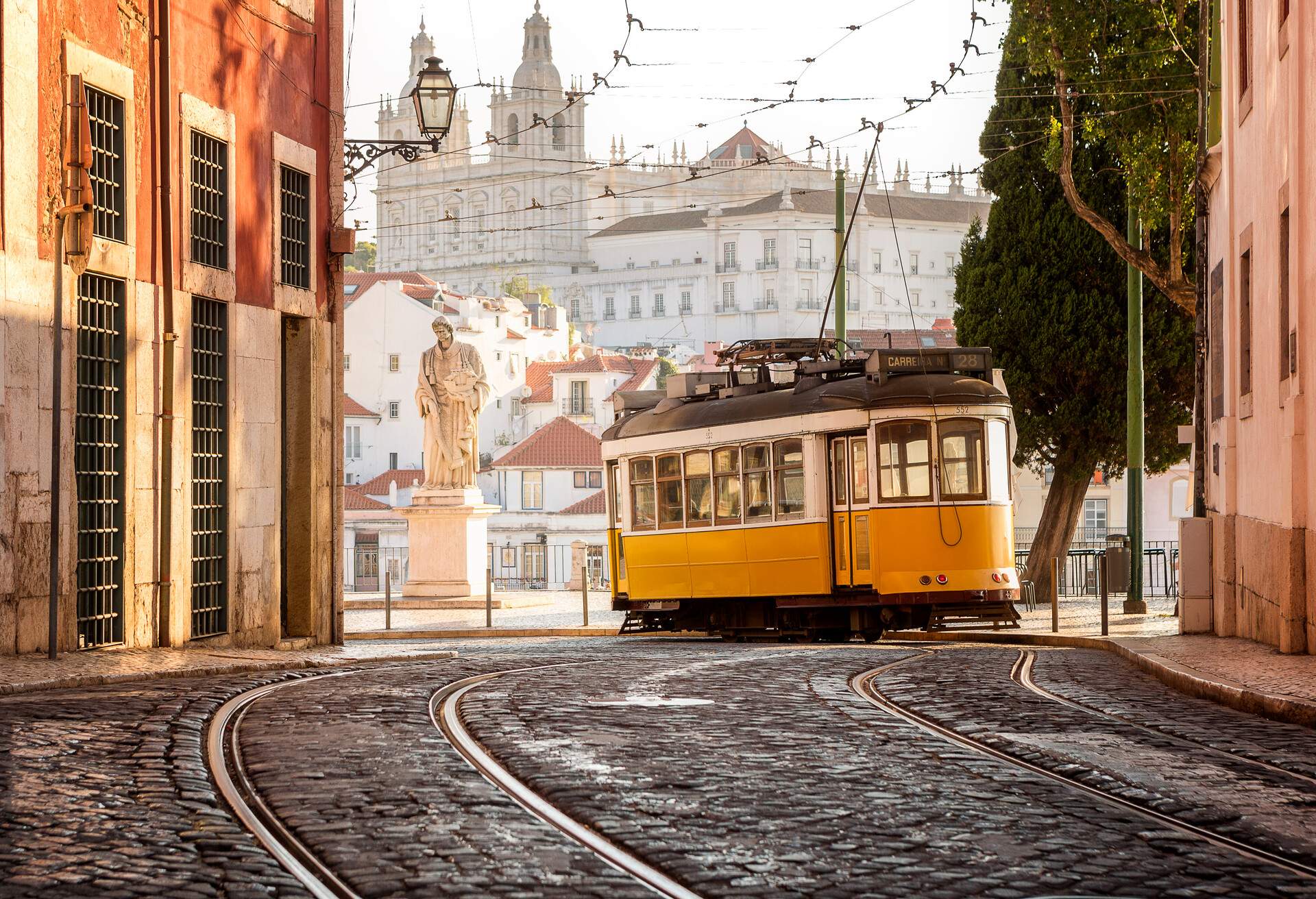 A yellow tram making its way into the city, passing by historic buildings.