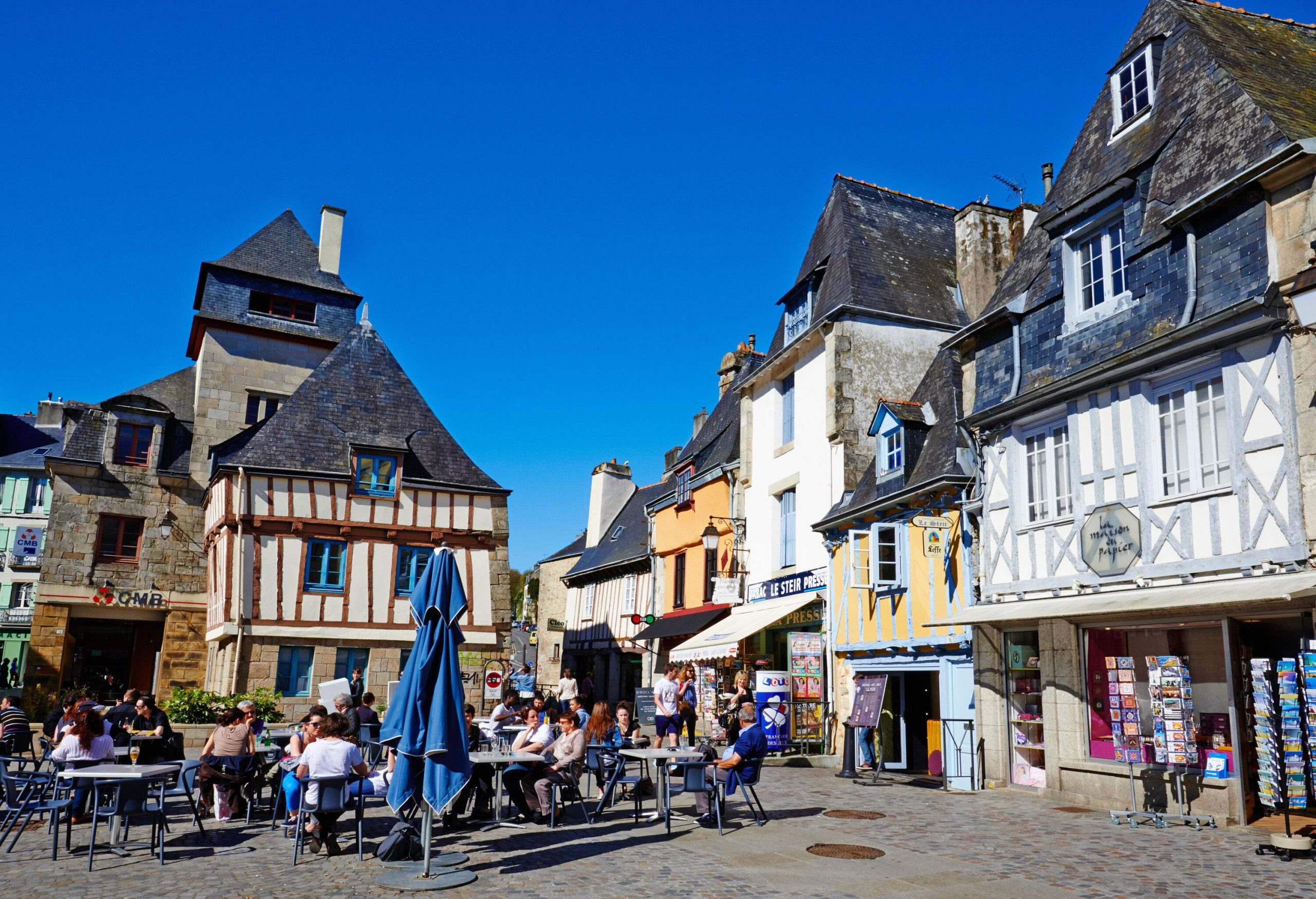 A lively town square with people dining outdoors in front of timber-framed structures.