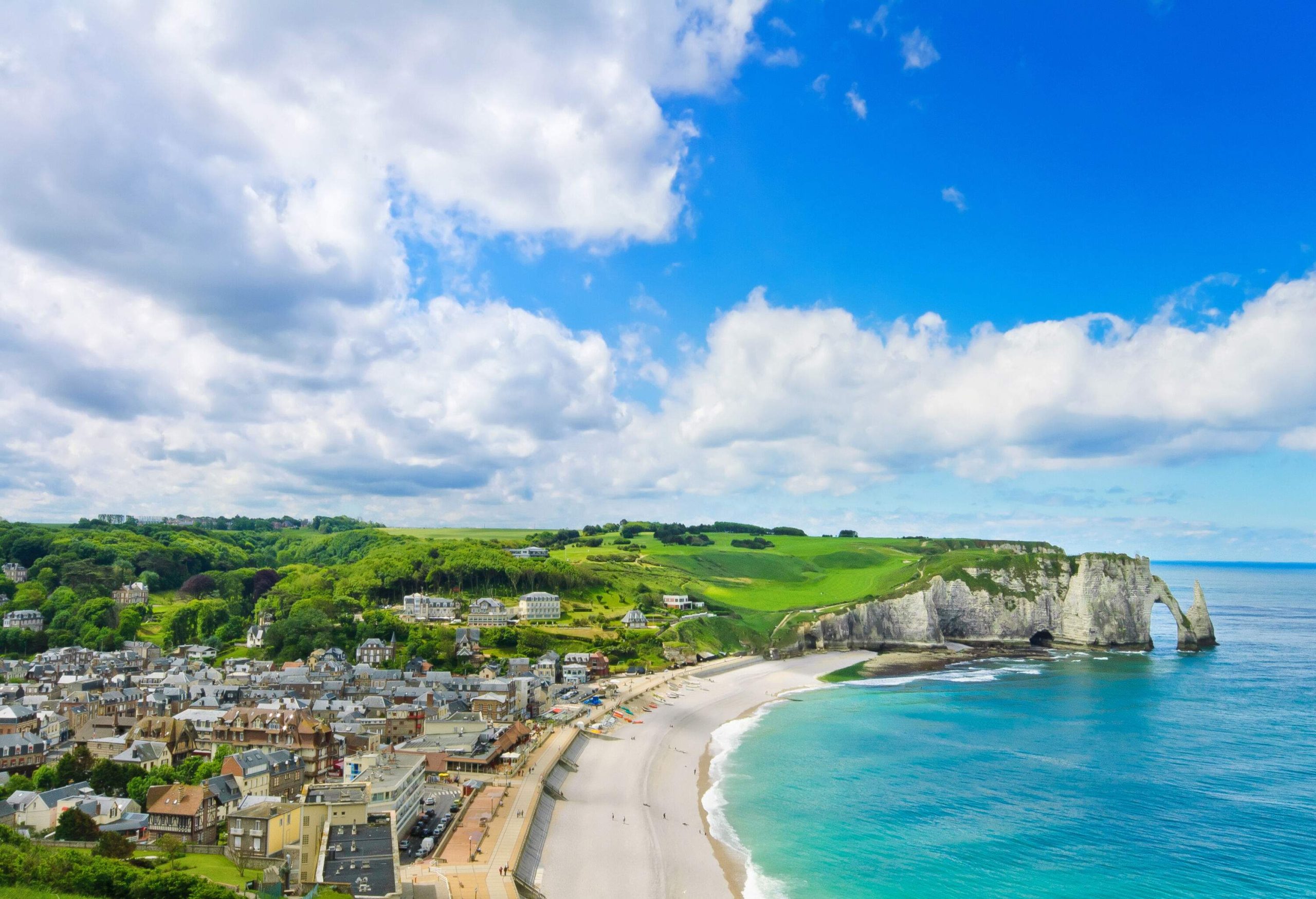 Aerial view of an old town by the sea on a lush island with an arch rock formation carved out of its verdant cliffs.