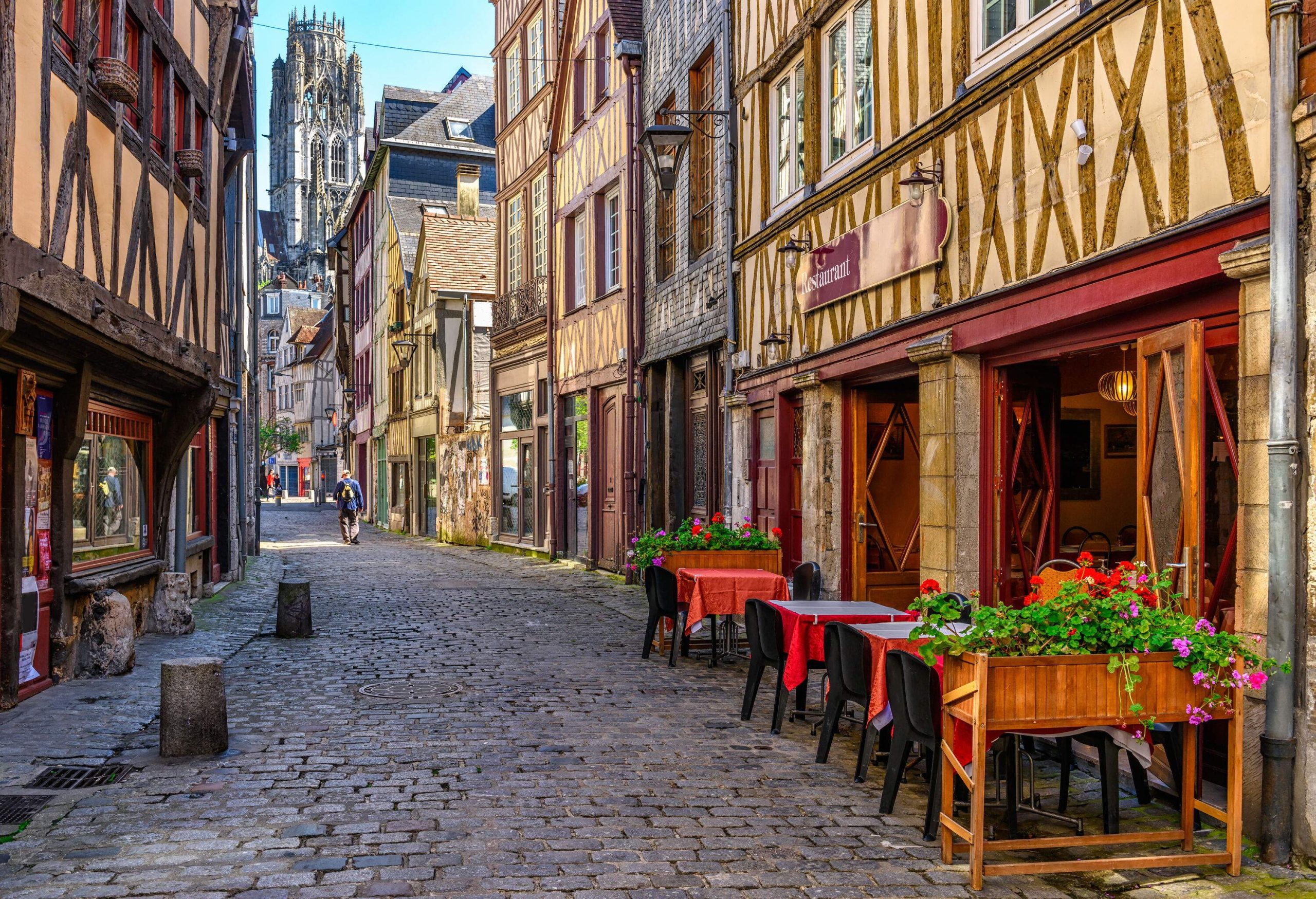 A man walking through a cozy cobbled street in the middle of traditional French half-timbered houses.