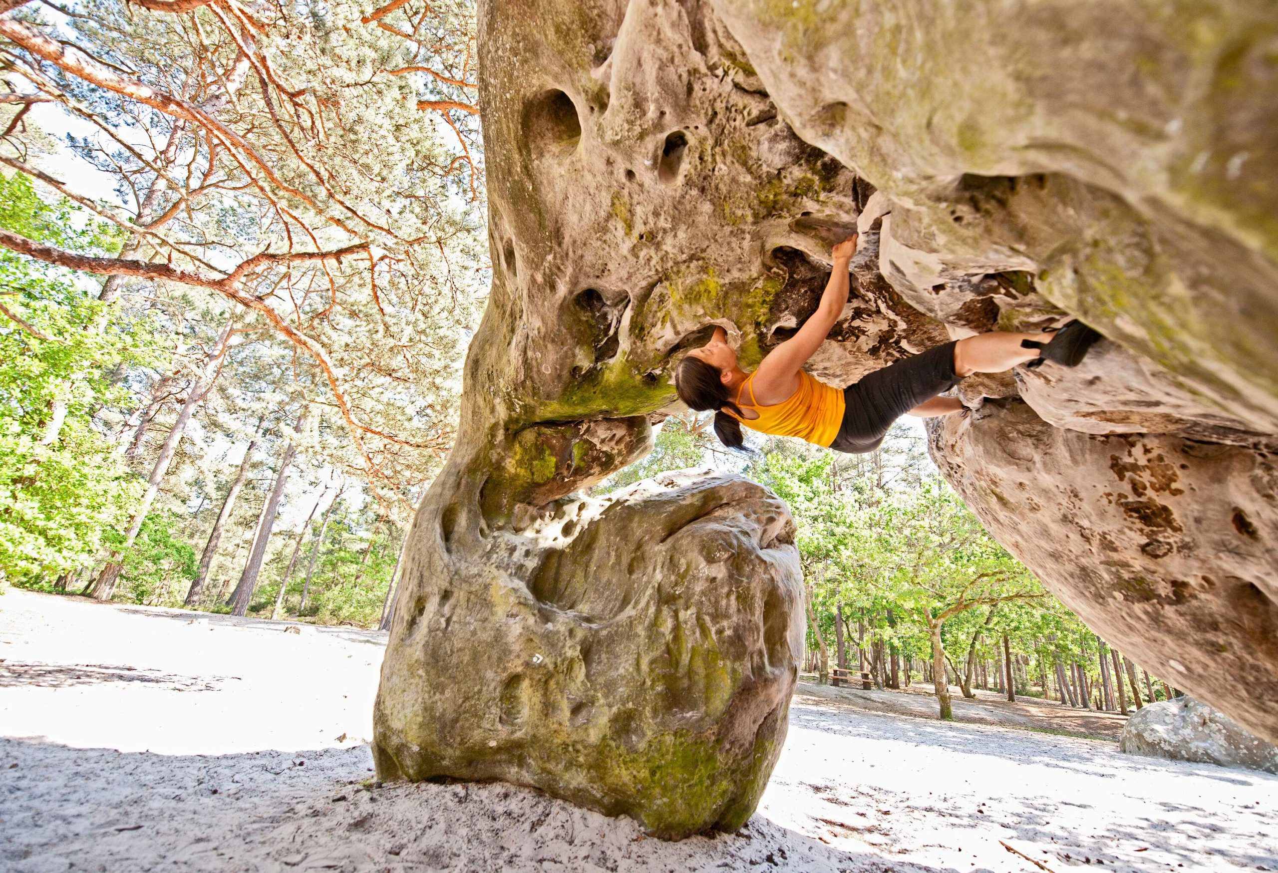 A fit lady climbs on a spectacular rock formation in the sunlit forest.