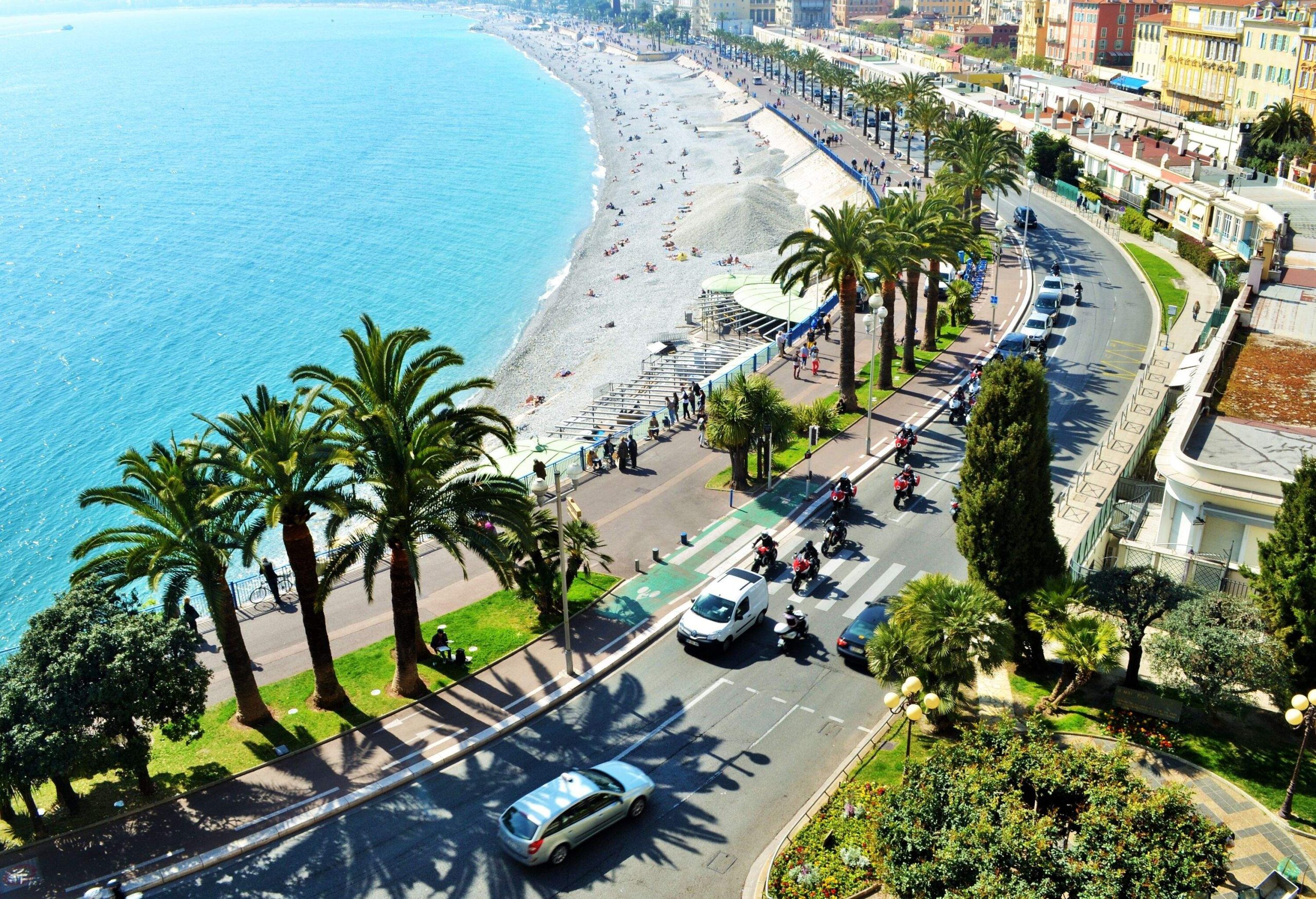 A crowded beach along a tree-lined promenade and highway.