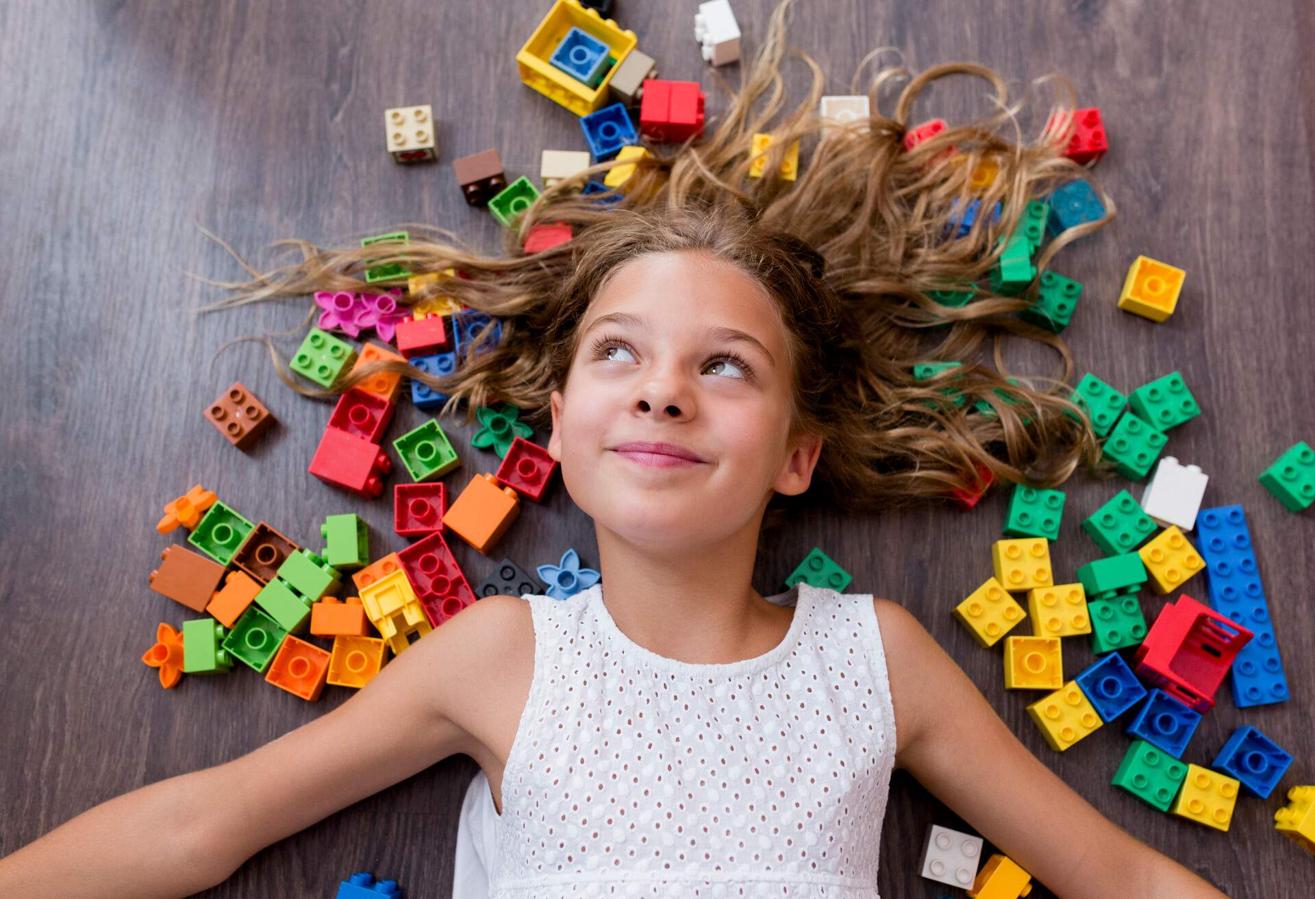 A girl in a white shirt lies on top of colourful Lego blocks.